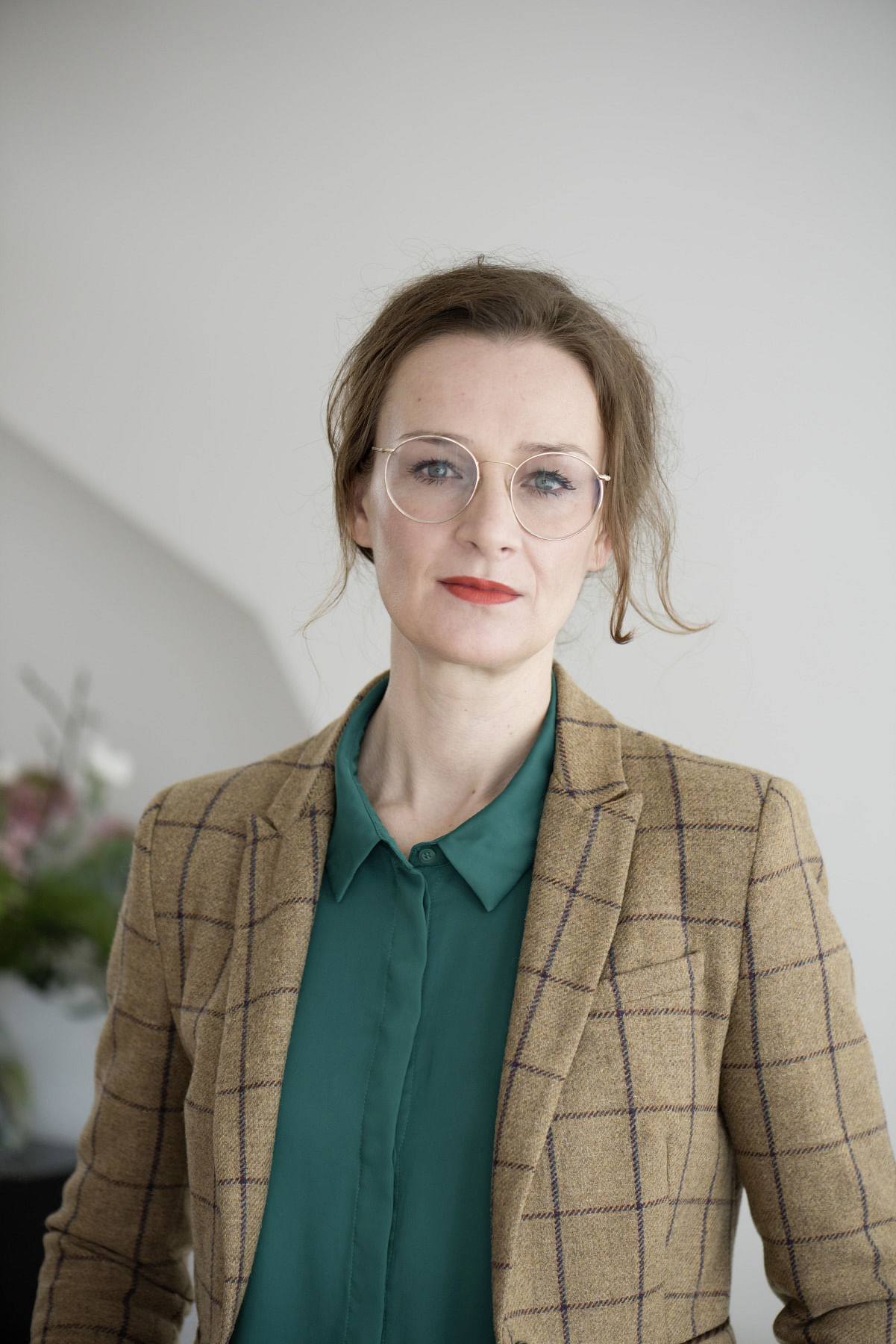 Die Autorin Franziska Schutzbach trägt ihr braunes Haar zurückgebunden, außerdem eine Metallbrille und dunkelroten Lippenstift, dazu ein grünes Hemd und einen karierten Blazer. Sie guckt selbstbewusst in die Kamera.