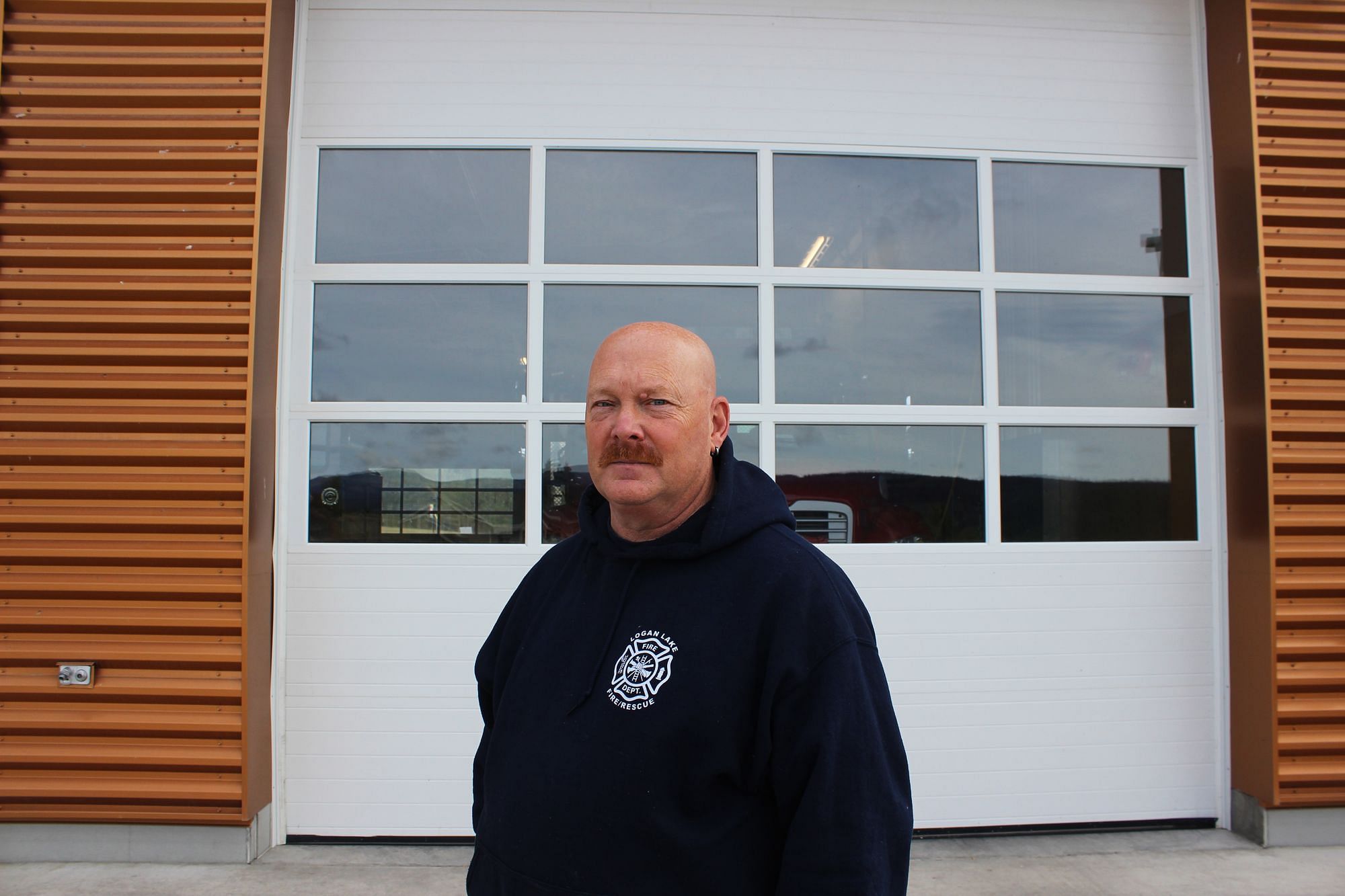 Doug Wilson, ein Mann mittleren Alters mit Glatze, vor seiner Feuerwache im Pulli der Feuerwehr.