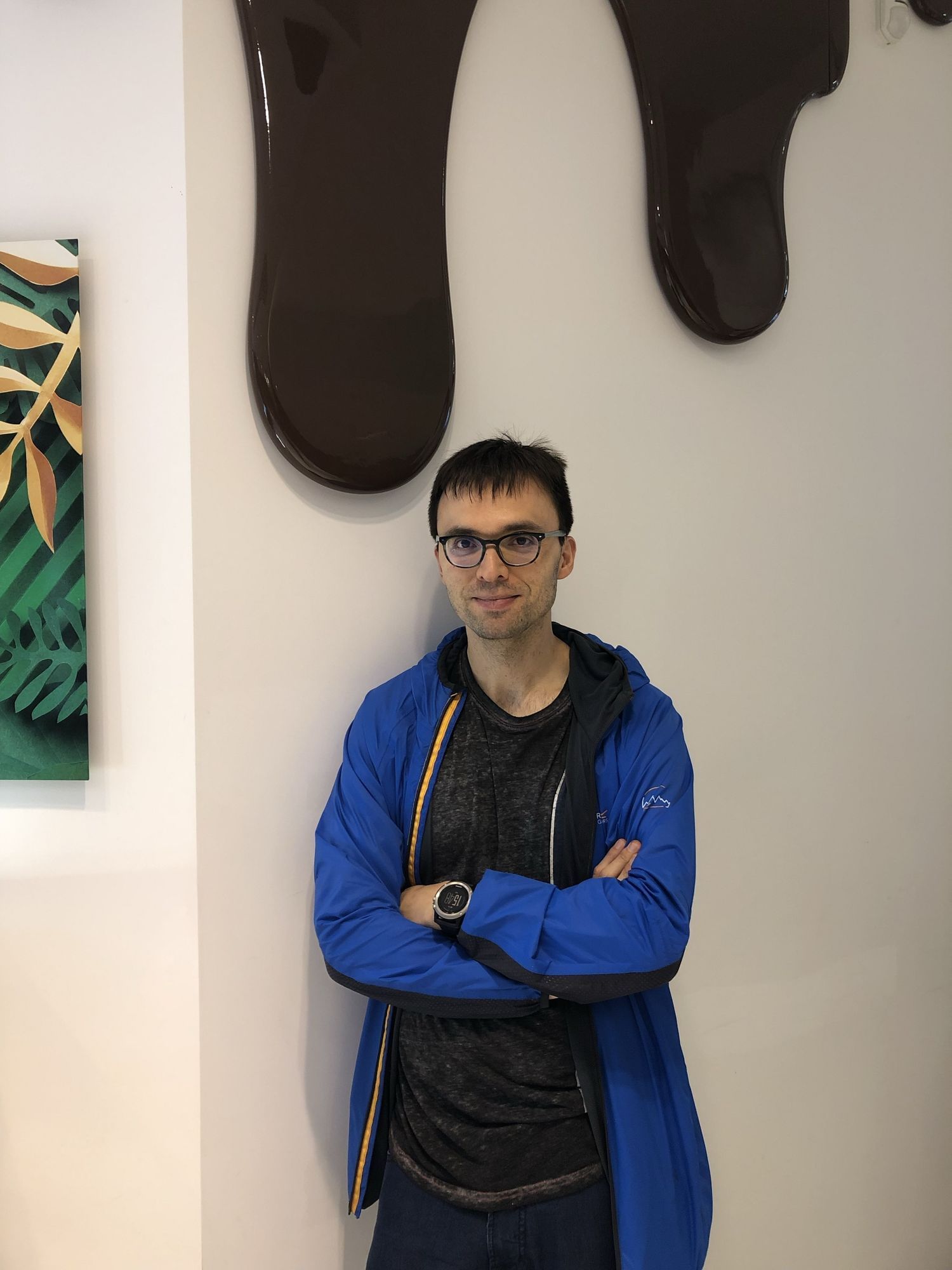 Salvo in einer blauen Jacke und schwarzen Hoodie, die Arme verschränkt, neutral in die Kamera blickend.