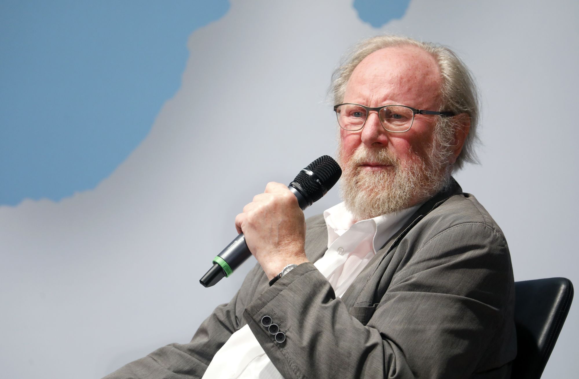 Wolfgang Thierse sitzt vor einem Himmelähnlichen Hintergrund, das Mikrofon in der Hand und aufmerksam zuhörend wenn gleich auch leicht verwirrt.