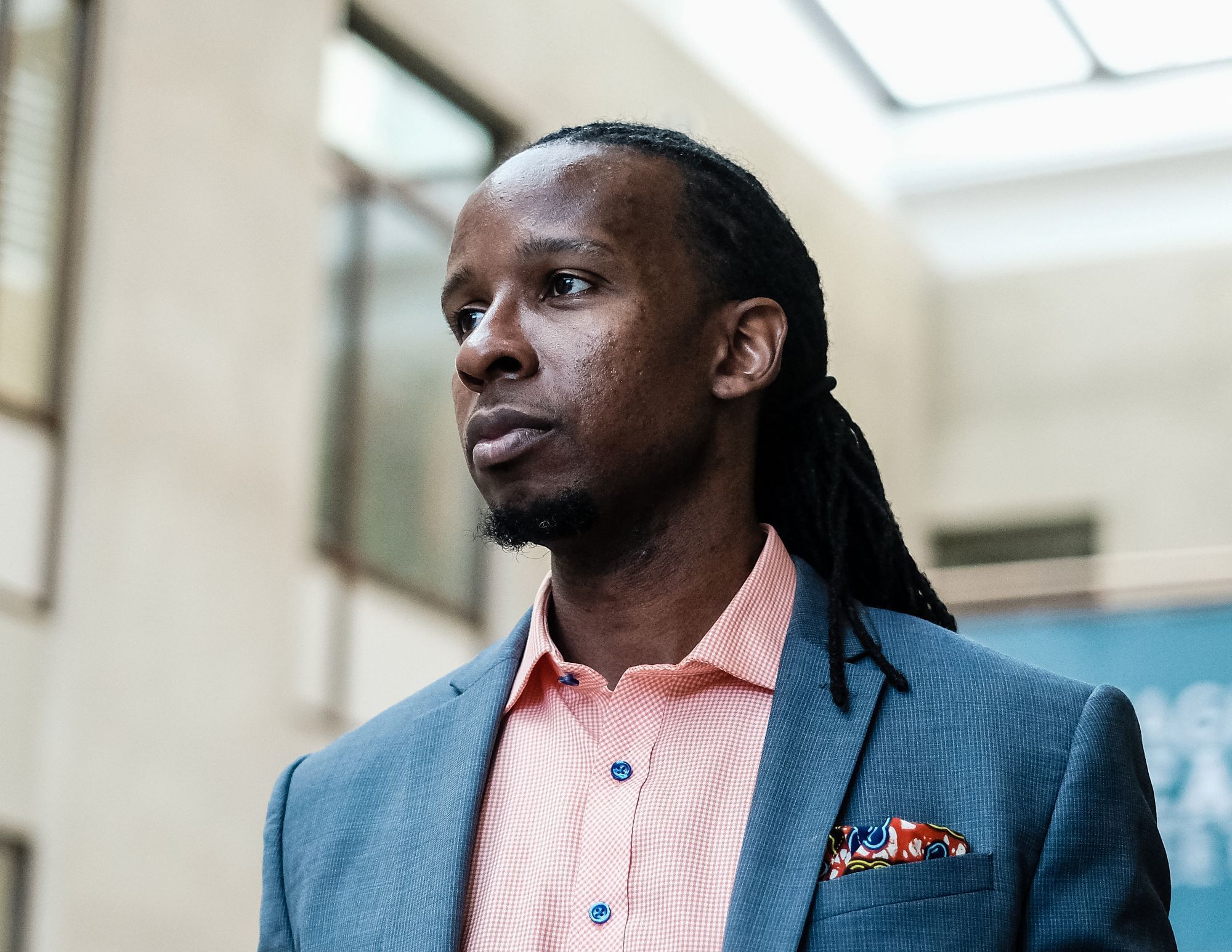 Porträt von Professor Dr. Ibram X. Kendi, er trägt ein rot weiß kariertes Hemd, ein duneklblau-meliertes Sacko, hat leichten Bart und geflochtete Haare im Stil von Braids.