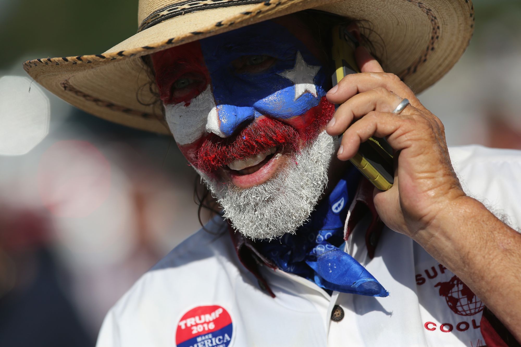 Ein Donald Trump Unterstützer telefoniert. Sein Gesicht ist in den Farben und Symbolen der Texanischen Flagge bemalt.
