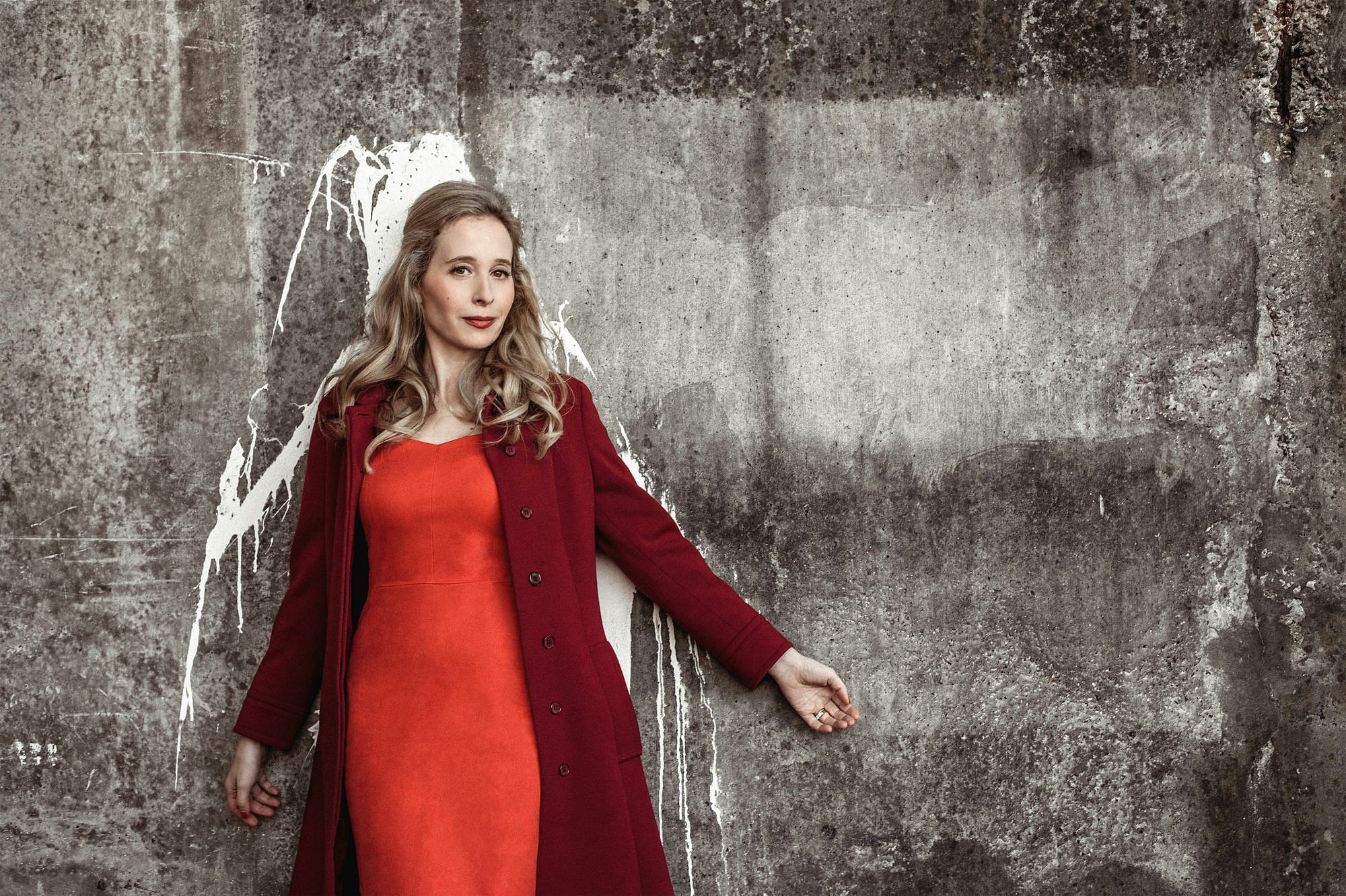 EIne Frau vor einer Betonwand, sie trägt ein rotes Kleid.