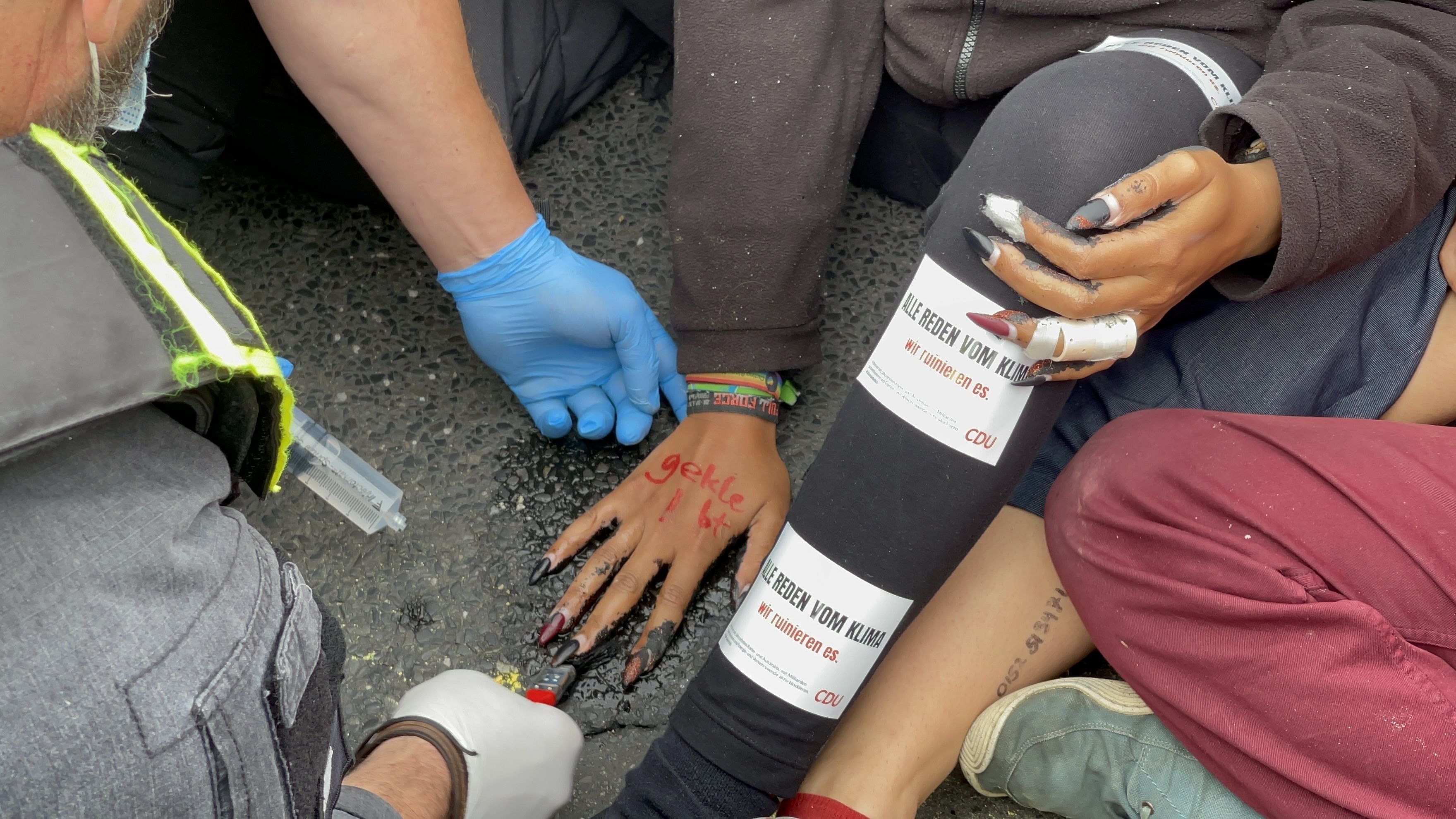 Eine Hand liegt in einer spiegelnden Lache, auf dem Handrücken steht "Geklebt".