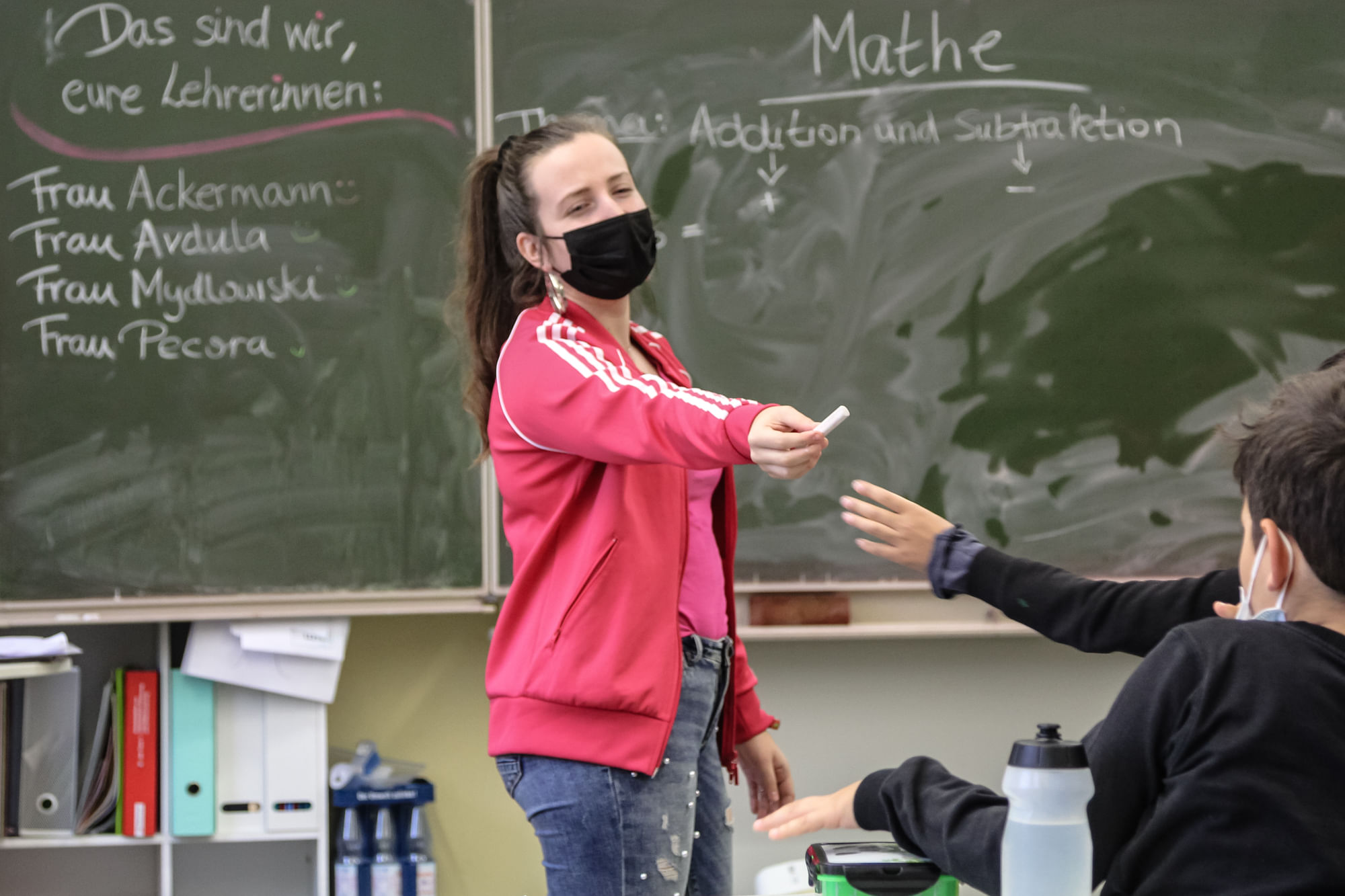 Laura Mydlowski reicht einem Schüler ein Stück Kreide.