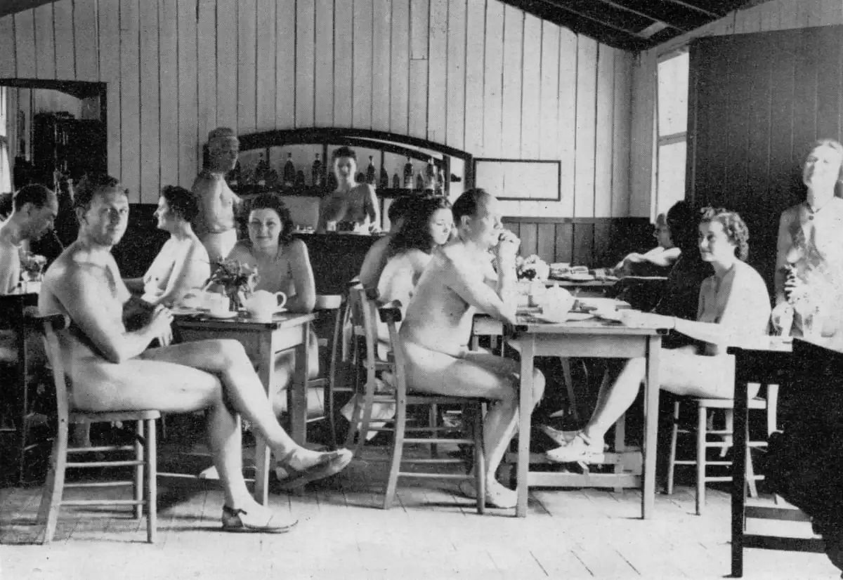 Schwarz-weiß Bild; Eine gemischte Gruppe von Frauen und Männern sitzen nackt in einem Cafe.
