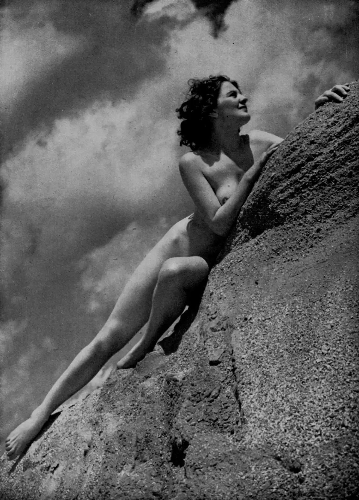 Eine nackte Frau liegt auf Steinen und blickt in den Himmel.