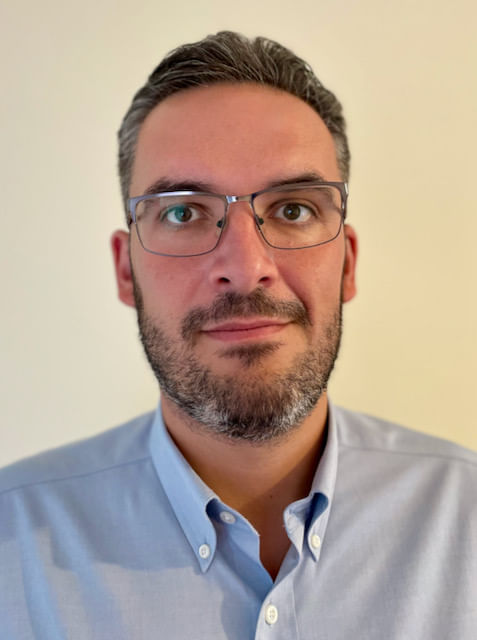 Porträt einer männlich gelesenen Person mit Brille und grau-melierten Haaren.
