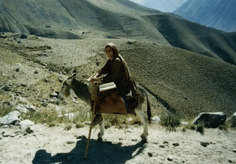Eine karge Berglandschaft und eine Frau auf einem Esel.
