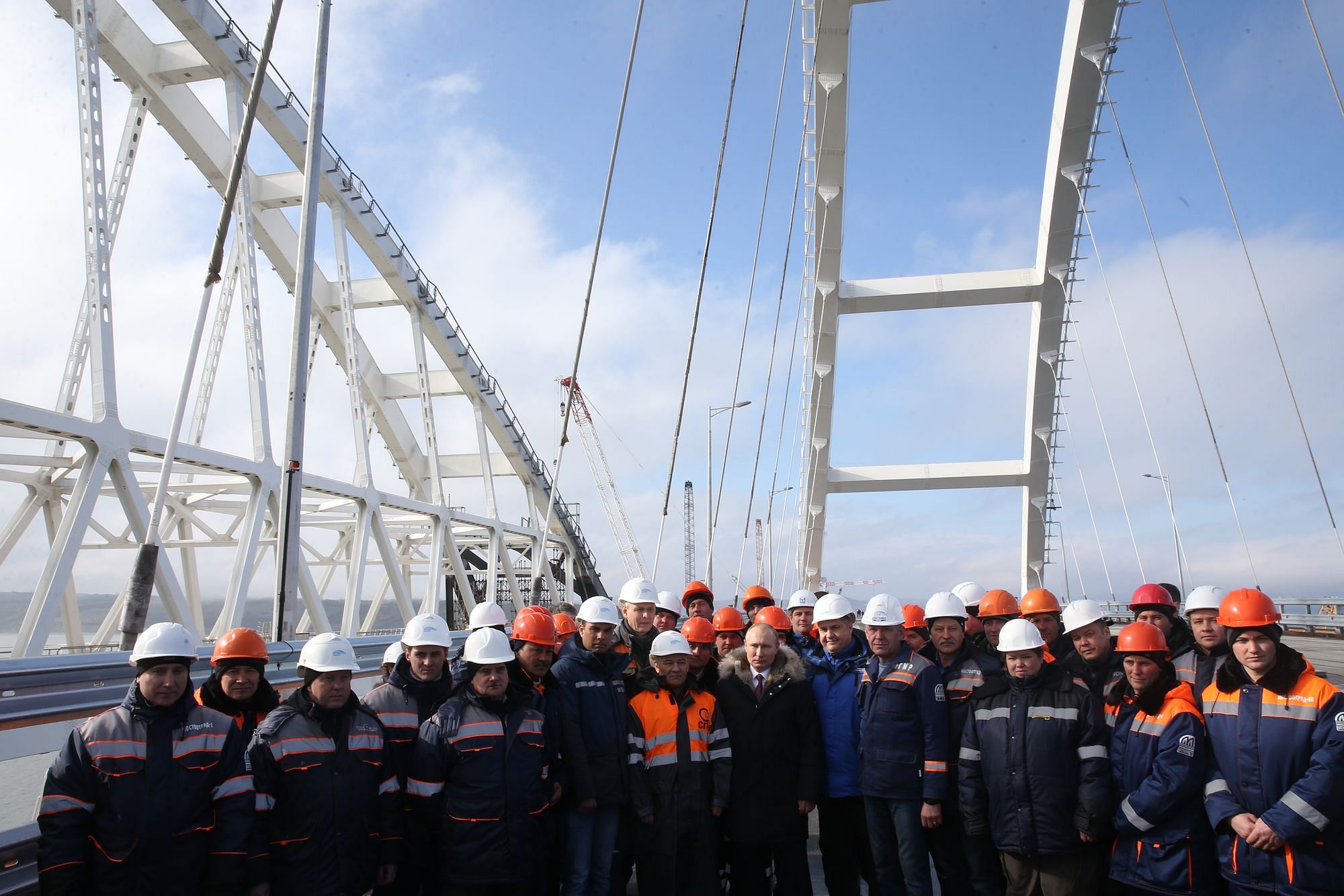 Der russische Präsident Wladimir Putin mit Arbeitern bei einem Besuch der Baustelle für die Krim-Brücke, unter den in Arbeit befindlichen Bögen der Brücke.
