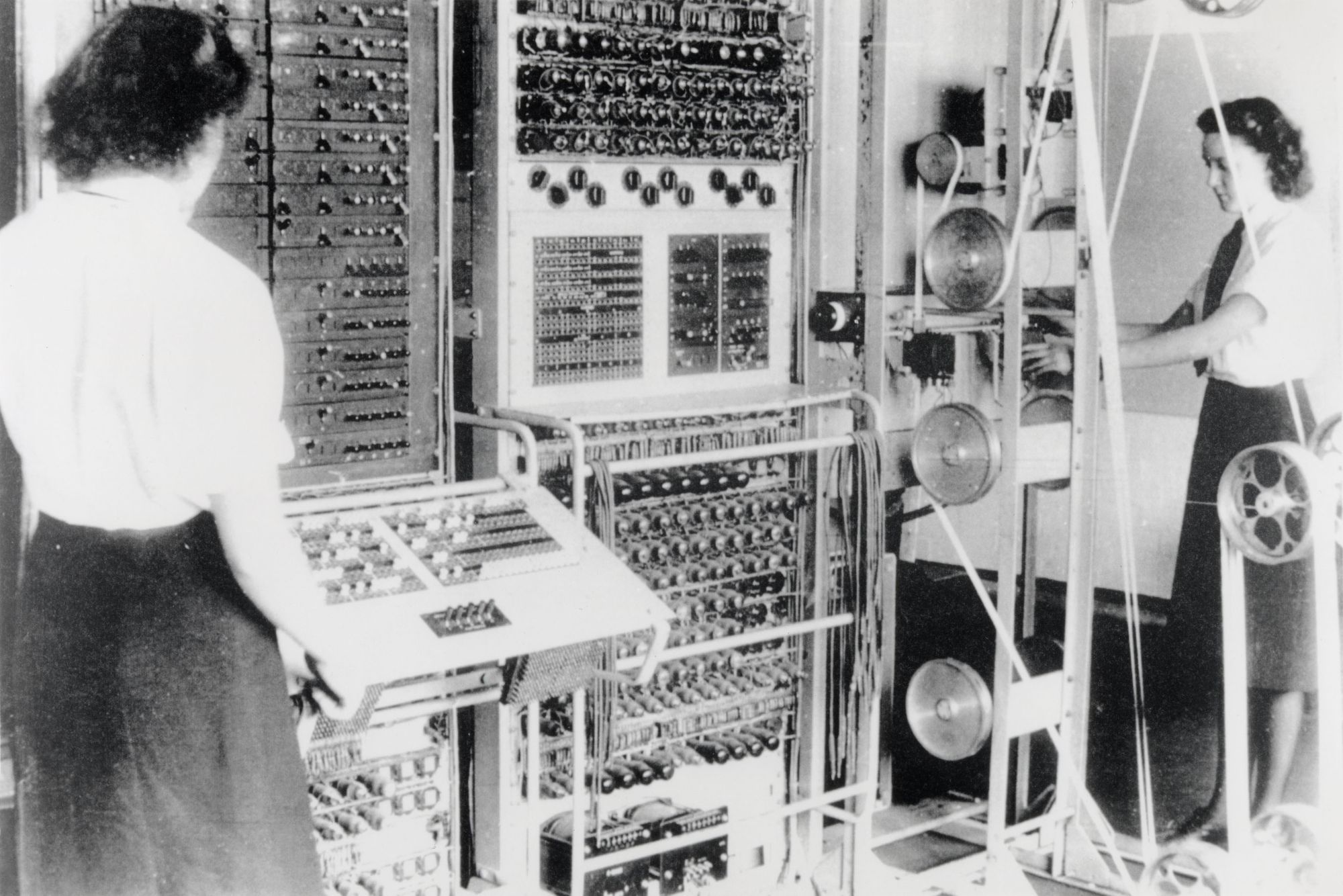 Viele Knöpfe und Apparate: Zwei Frauen bedienen einen großen altertümlichen Computer