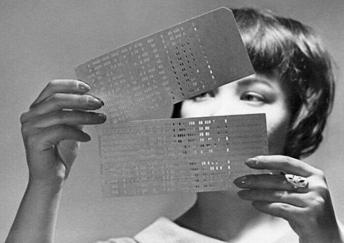 Frau, die auf ein Papier mit Löchern schaut. Dieses Papier steuerte früher Computer.