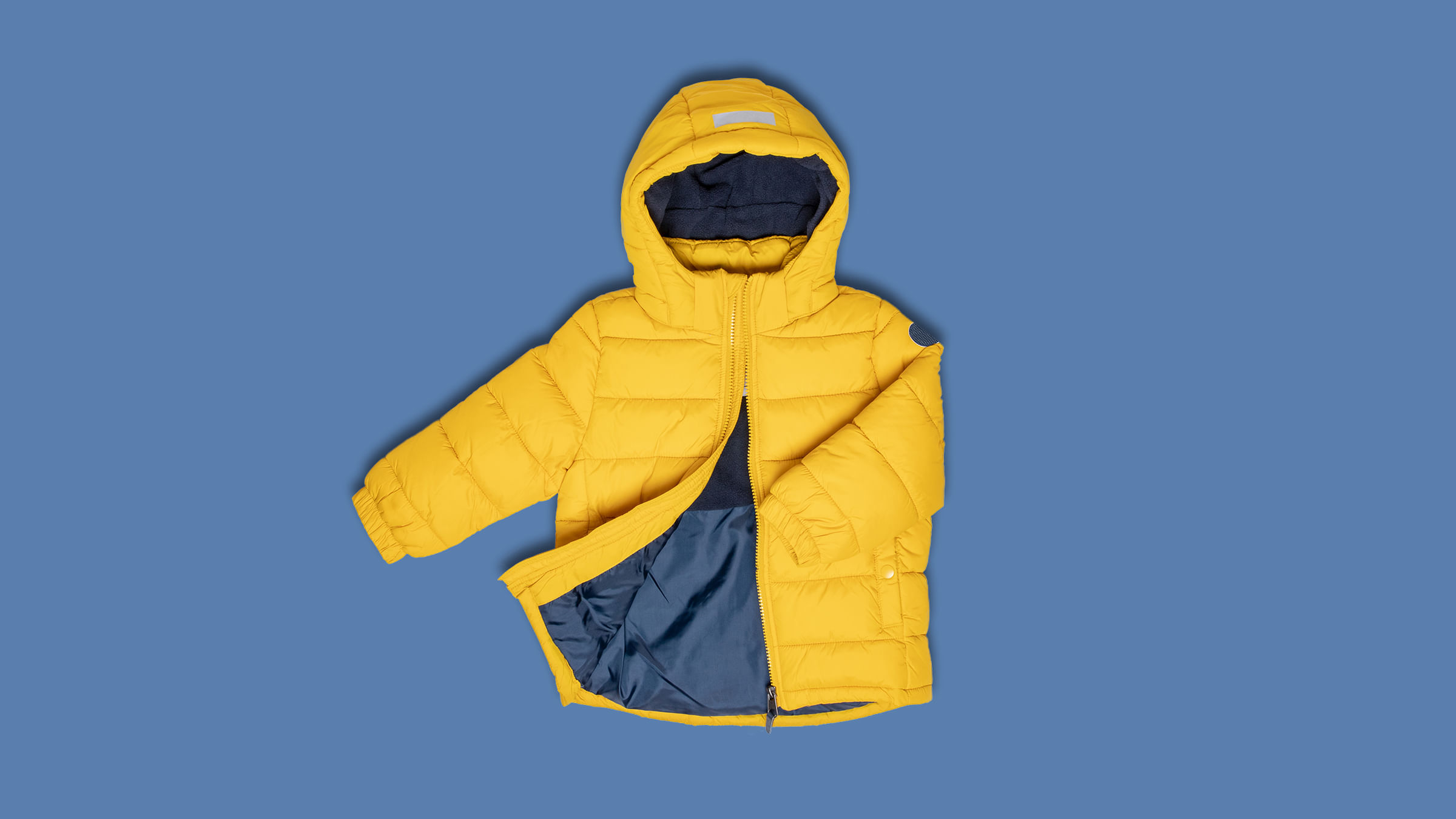 Eine Gelbe Daunenjacke liegt auf blauem Hintergrund