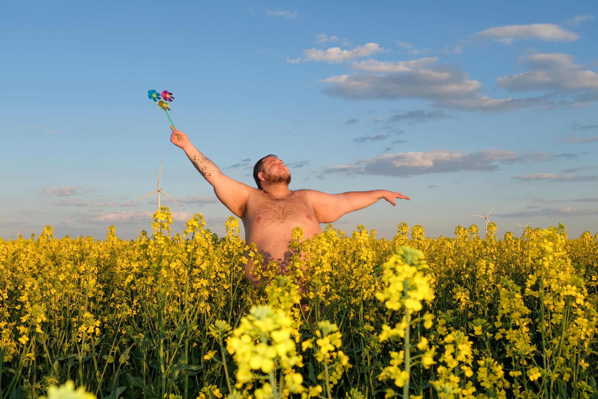 Wir sehen einen Mann, der (Oberkörper) nackt in einem Blumenfeld steht und das Gesicht in die Sonne hält.