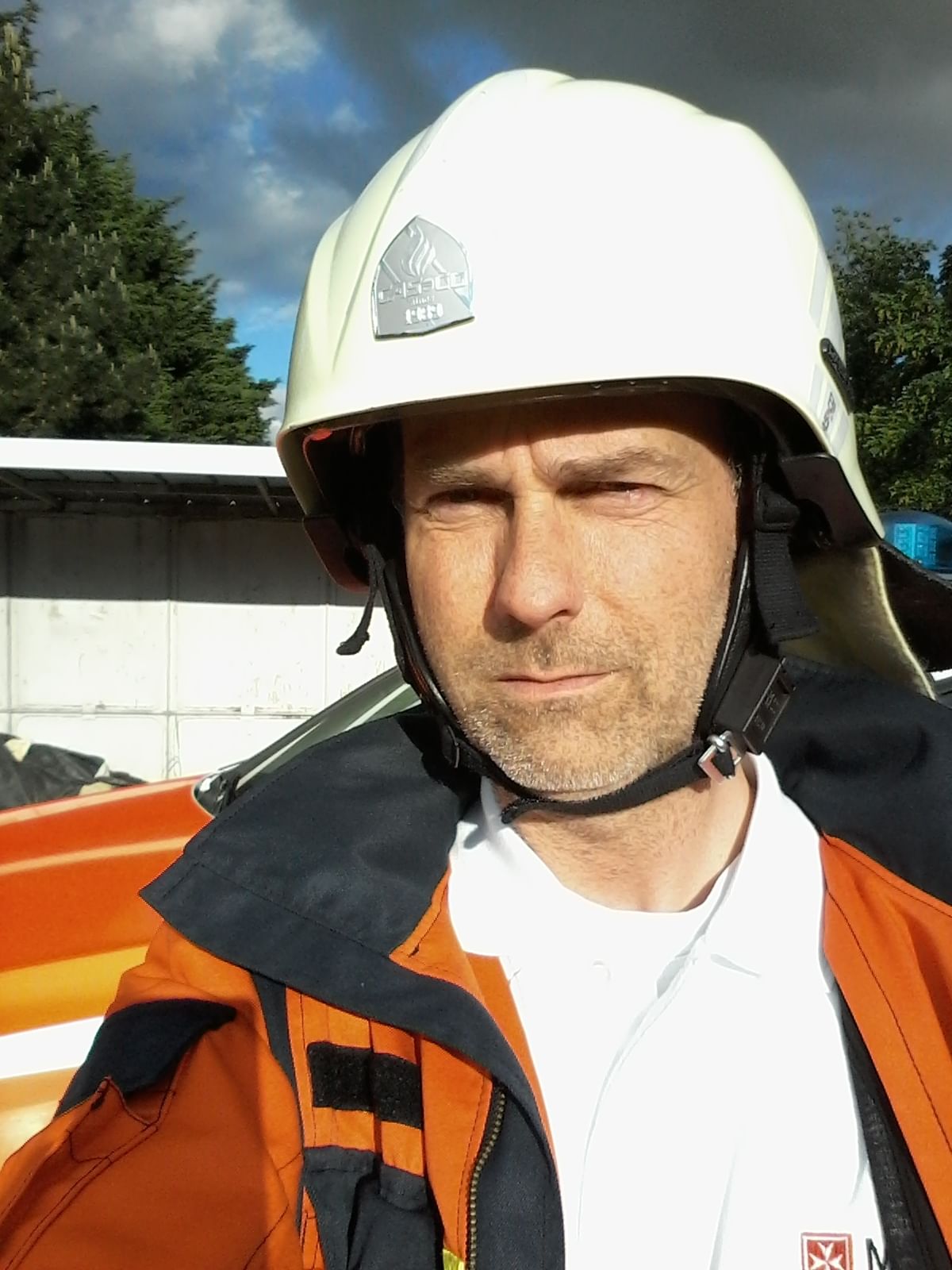 Ein Mann blickt in die Kamera. Er trägt die Uniform der Malteser und einen weißen Helm auf dem Kopf.
