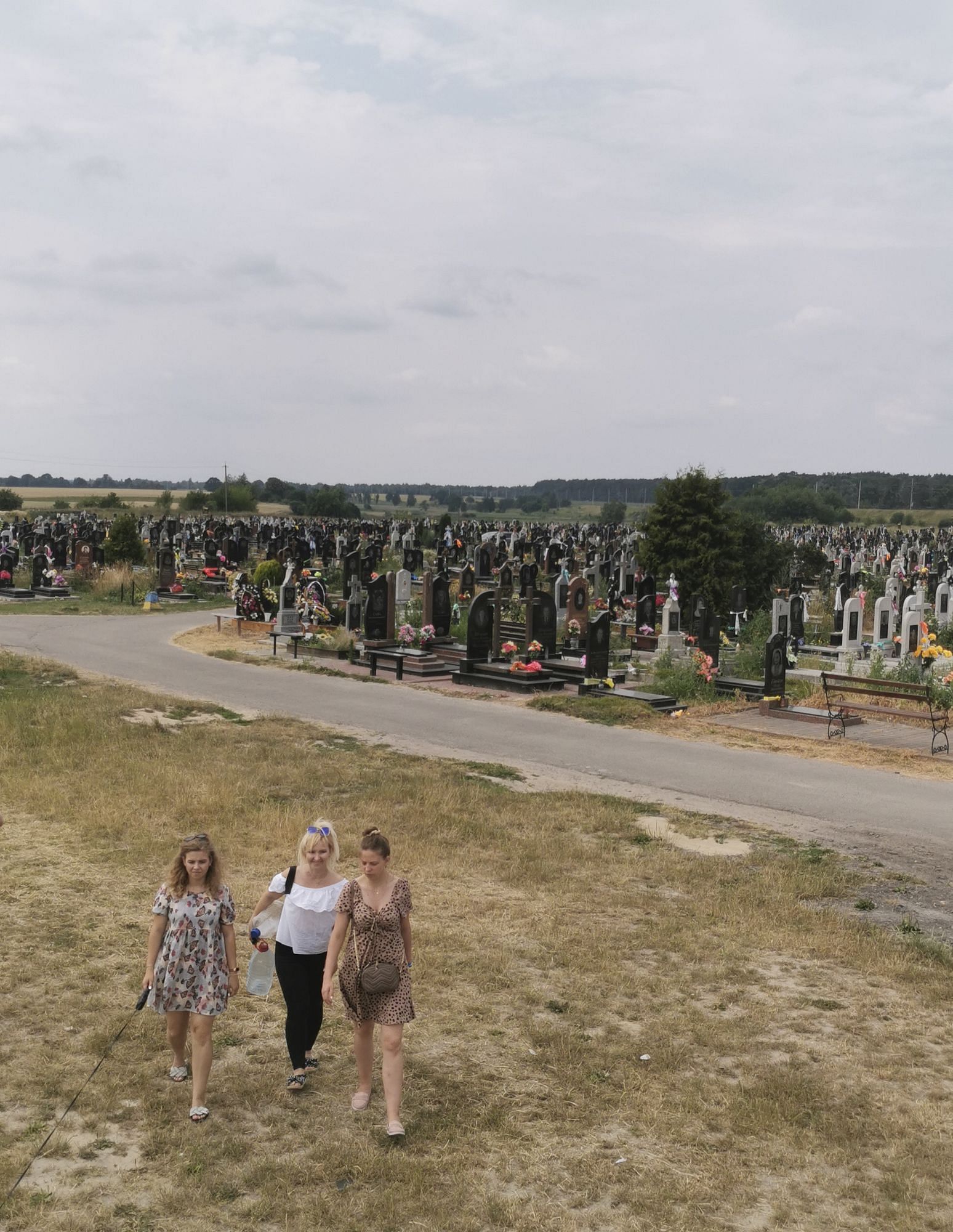 Drei Frauen laufen über den Friedhof. Im Hintergrund sind viele Gräber zu sehen.