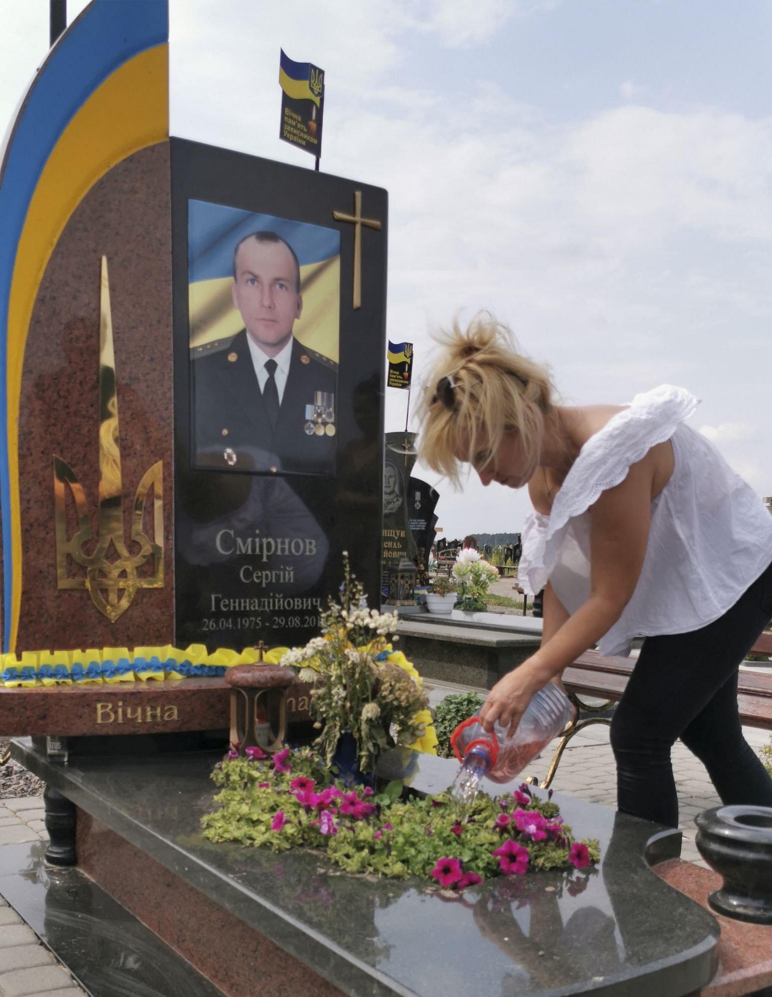 Eine Frau gießt die Blumen am Grab ihres Mannes. Ein Foto von ihm ist in den Grabstein eingearbeitet. Er war Soldat.