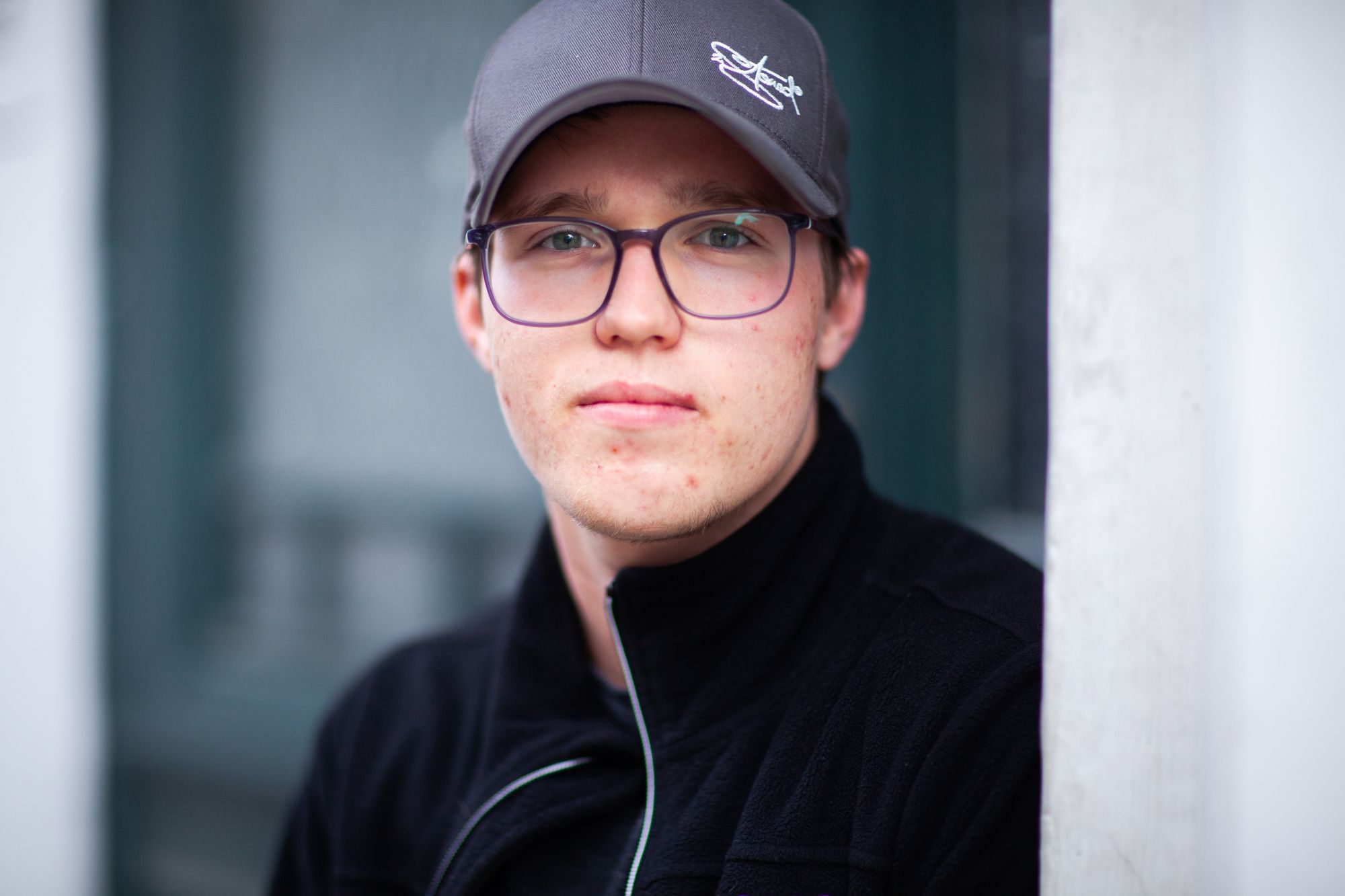 Wir sehen einen jungen Mann, der mit Baseballcap in die Kameraschaut.