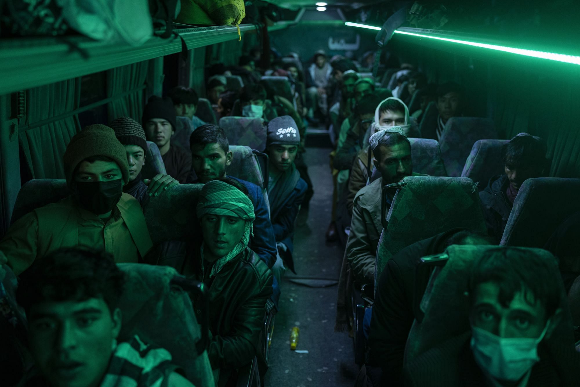 Innenaufnahme eines Busses bei Nacht. Viele Männer sitzen darin. Sie sind in grünes Licht getaucht.