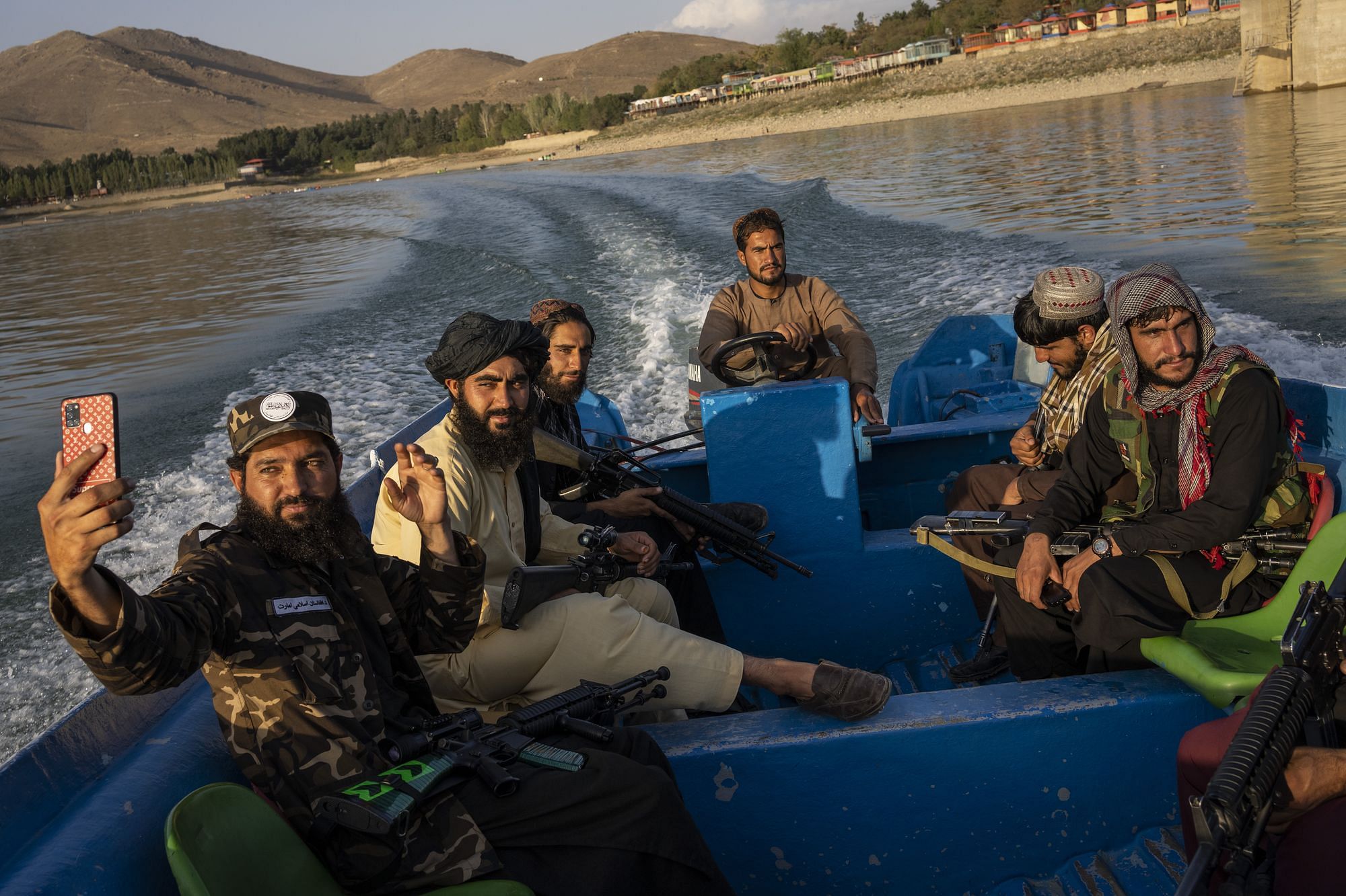 Sieben Taliban sind auf einem blauen Boot zu sehen. Sie tragen Waffen bei sich. Einer von ihnen macht ein Selfie mit seinem Handy.