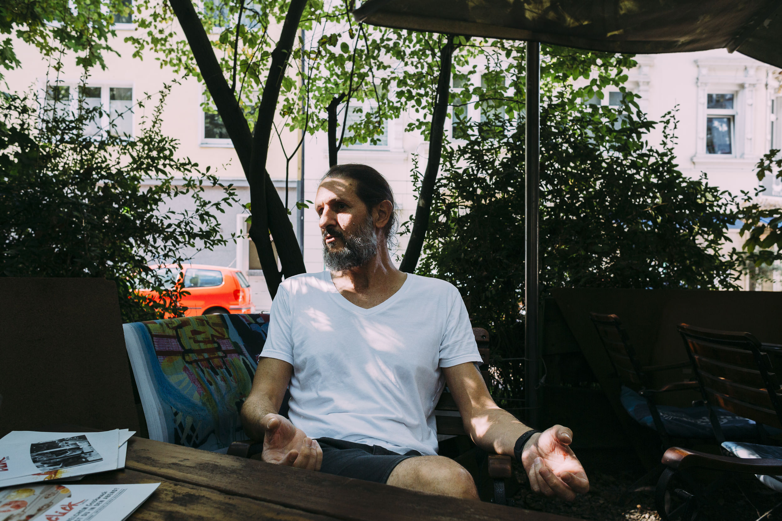 Saad sitzt in einem Biergarten. Er erzählt und gestikuliert.