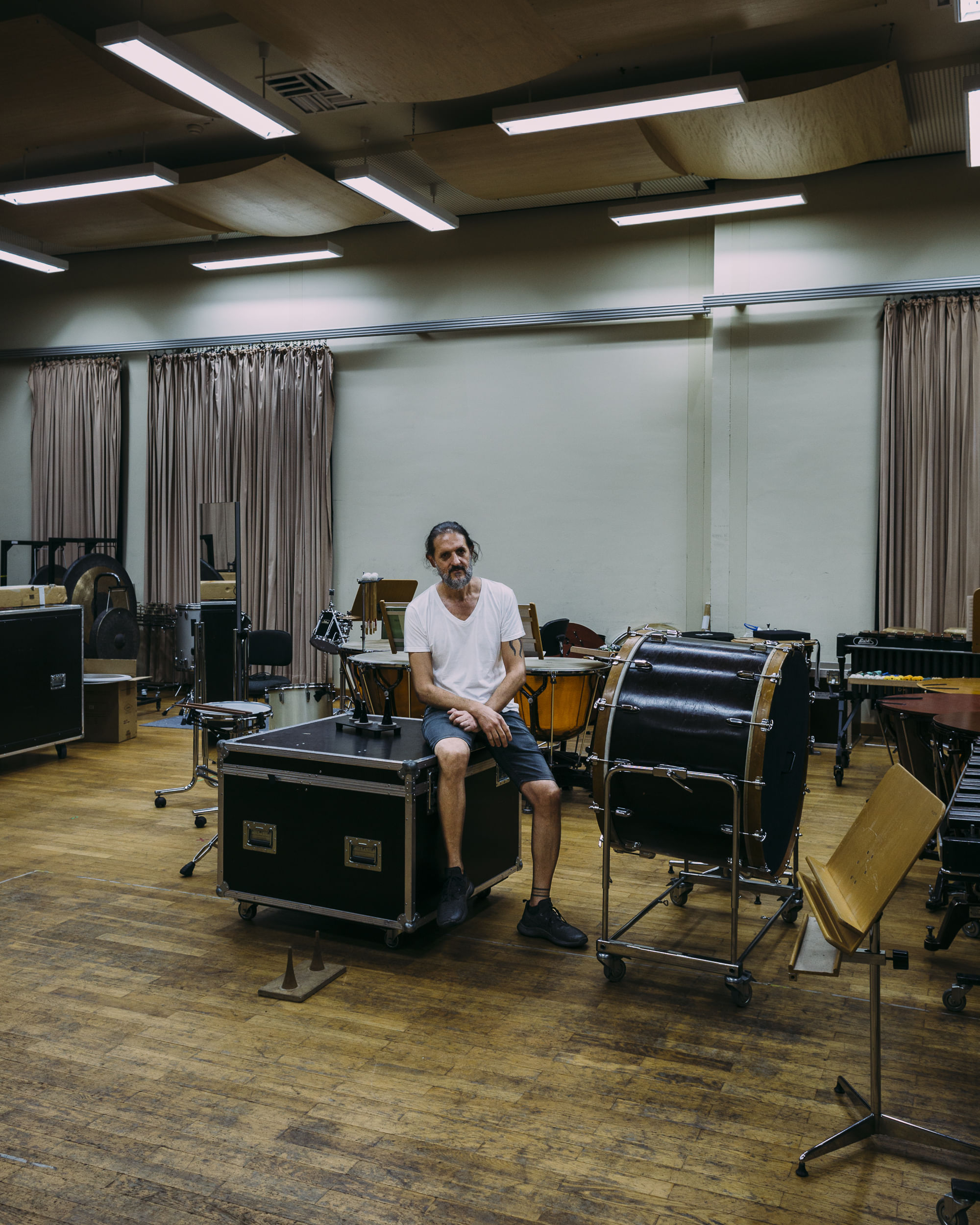 Saad sitzt auf einem Kasten im Instrumentenraum, umgeben von Instrumenten und Notenständern.