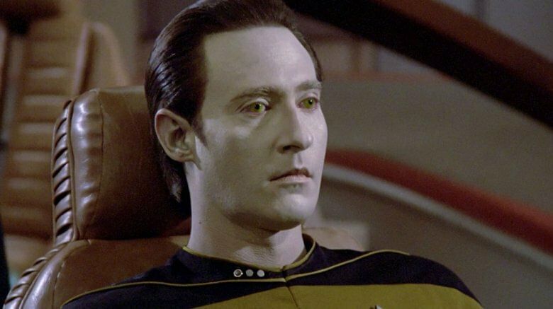 Mr. Data sitzt auf einen Stuhl und starrt in die Ferne.