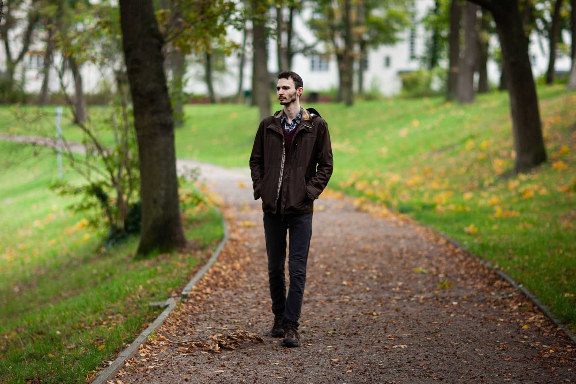Adam läuft. durch einen Park. Er trägt eine braune Jacke und eine schwarze Hose.