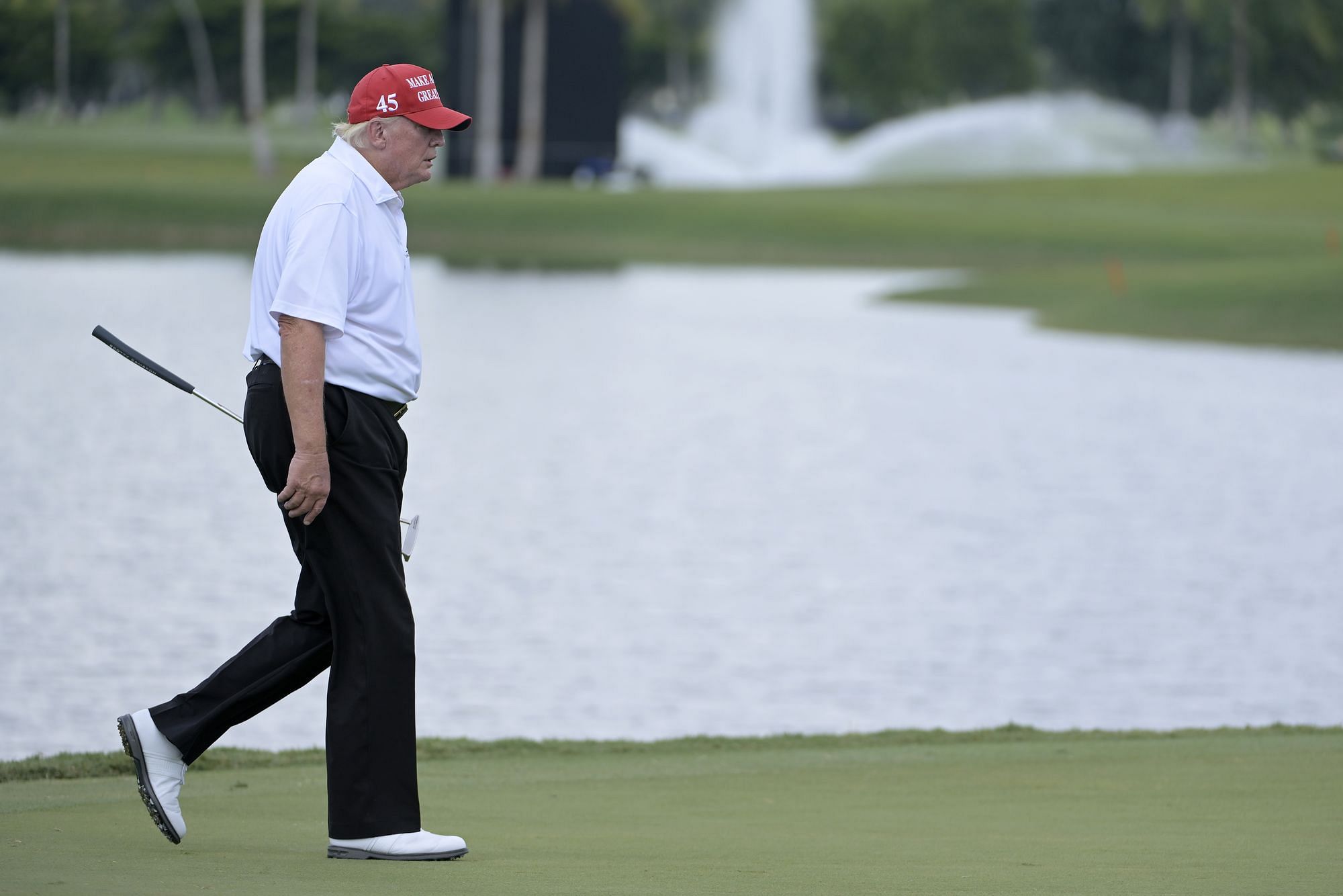Trump läuft über den Golfplatz, in der Hand seinen Schläger und auf dem Kopf eine rote Mütze.