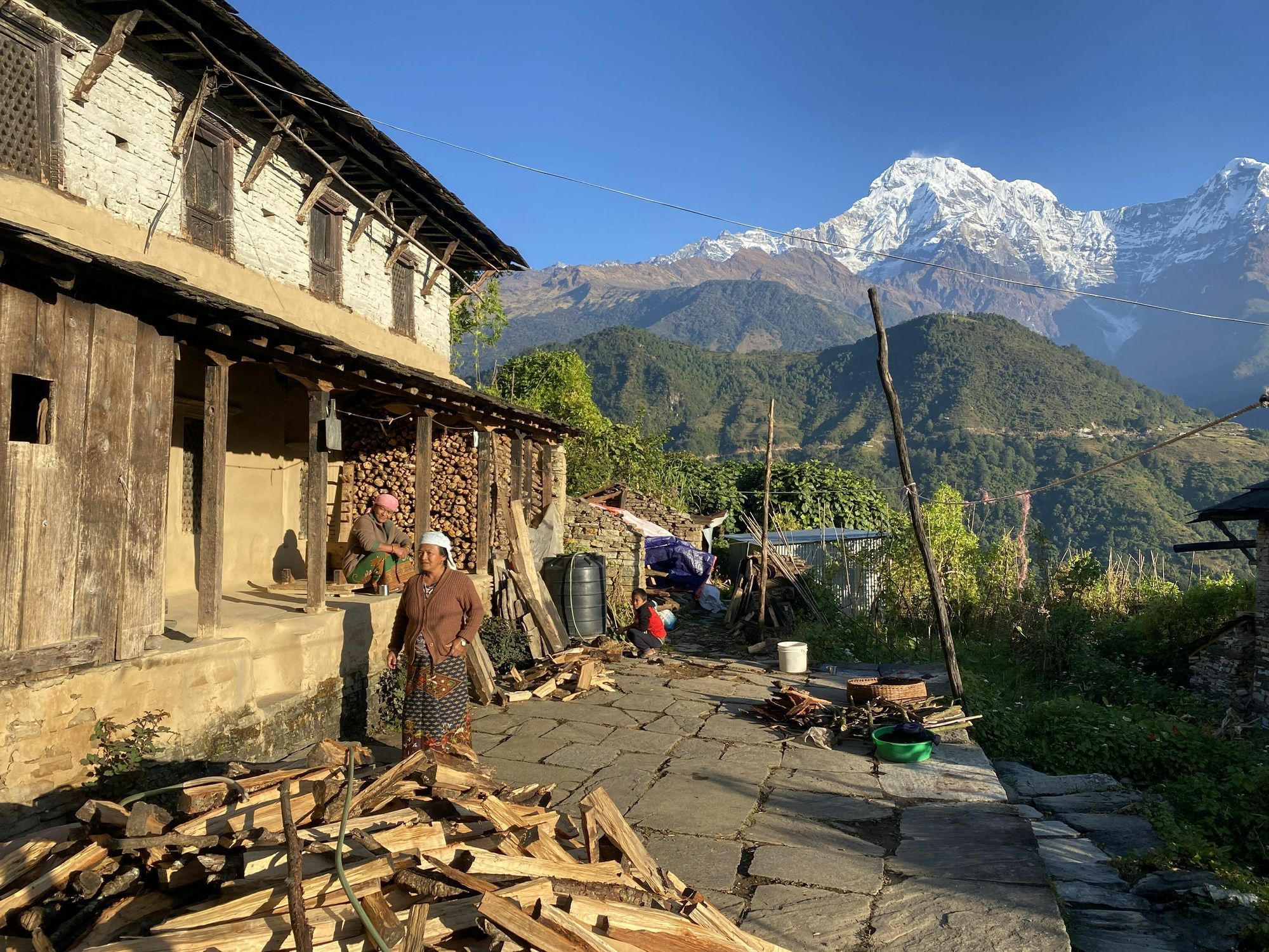 Ein Haus in Seitenansicht, im Hintergrund sind Berge. Eine Frau steht davor.