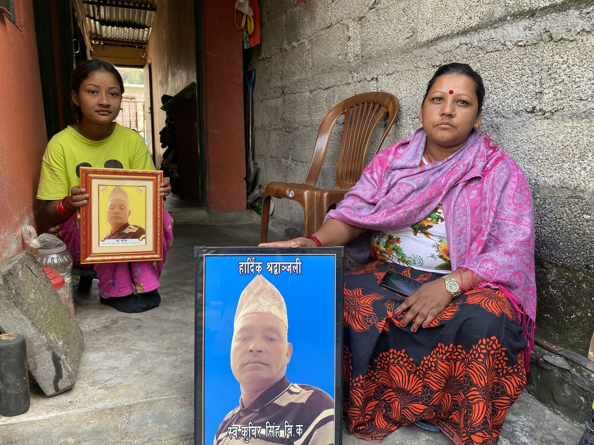 Eine Frau und ein Mädchen sitzen im Hauseingang. Sie halten Portraits eines Mannes.