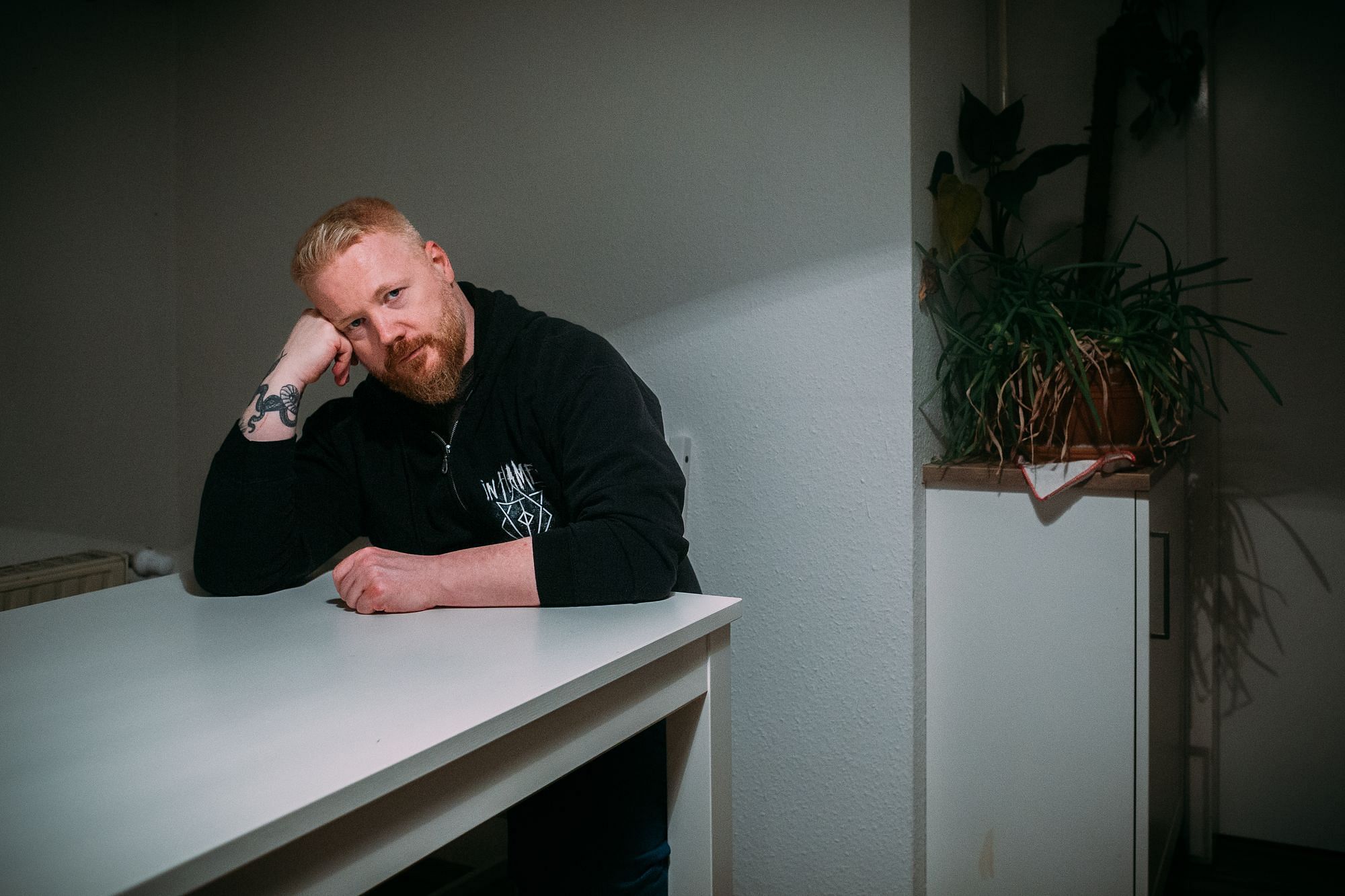 Martin sitzt am Küchentisch, er stützt seinen Kopf auf seinem rechten Arm ab. Im Hintergrund sind ein paar Pflanzen zu sehen.