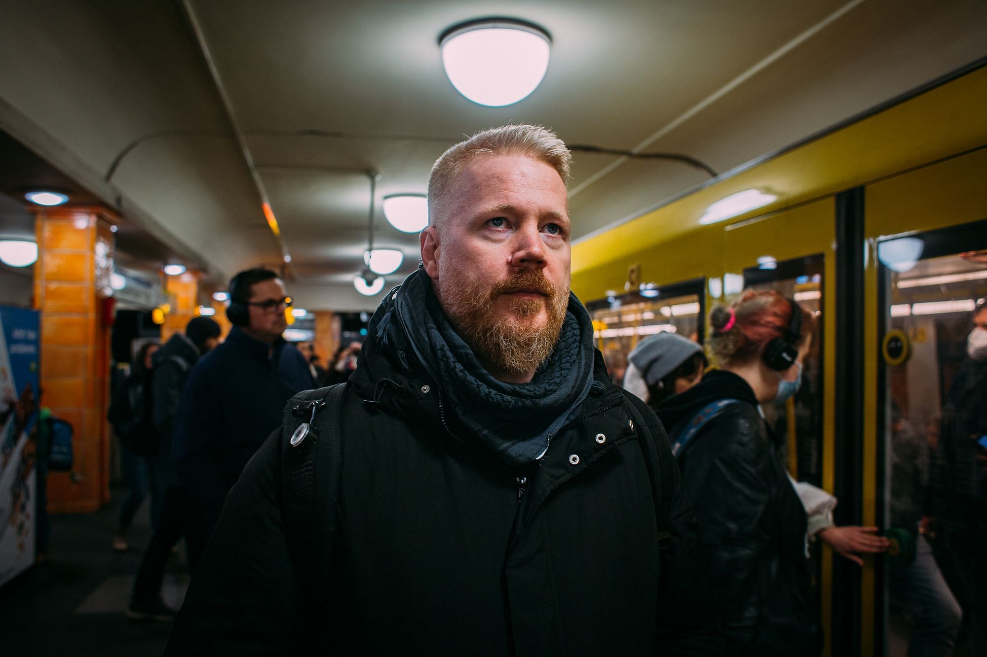 Martin steht in einer U-Bahn-Station und blickt sich um. Eine Bahn ist gerade eingefahren, Menschen steigen ein und aus.