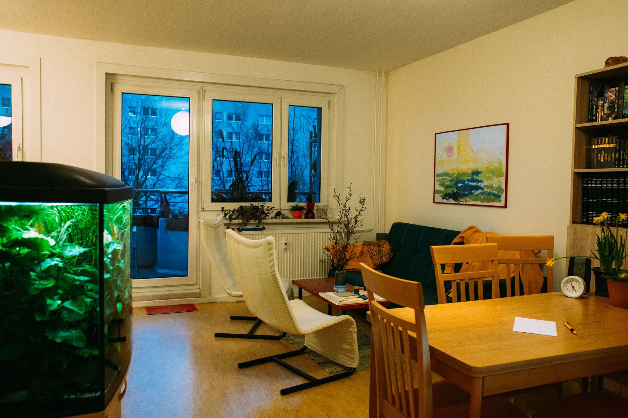 Zu sehen ist das Wohnzimmer in der Wohnung von Karin und Co. Links ein Aquarium, rechts ein heller, aufgeräumter Esstisch. Dahinter eine Couch und zwei weiße Sessel.