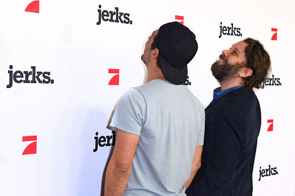 Christian Ulmen und Fahri Yardim stehen mit dem Rücken zur Kamera und gucken auf eine Wand, auf der "Jerks" steht und das Logo von Pro7 zu sehen kst.