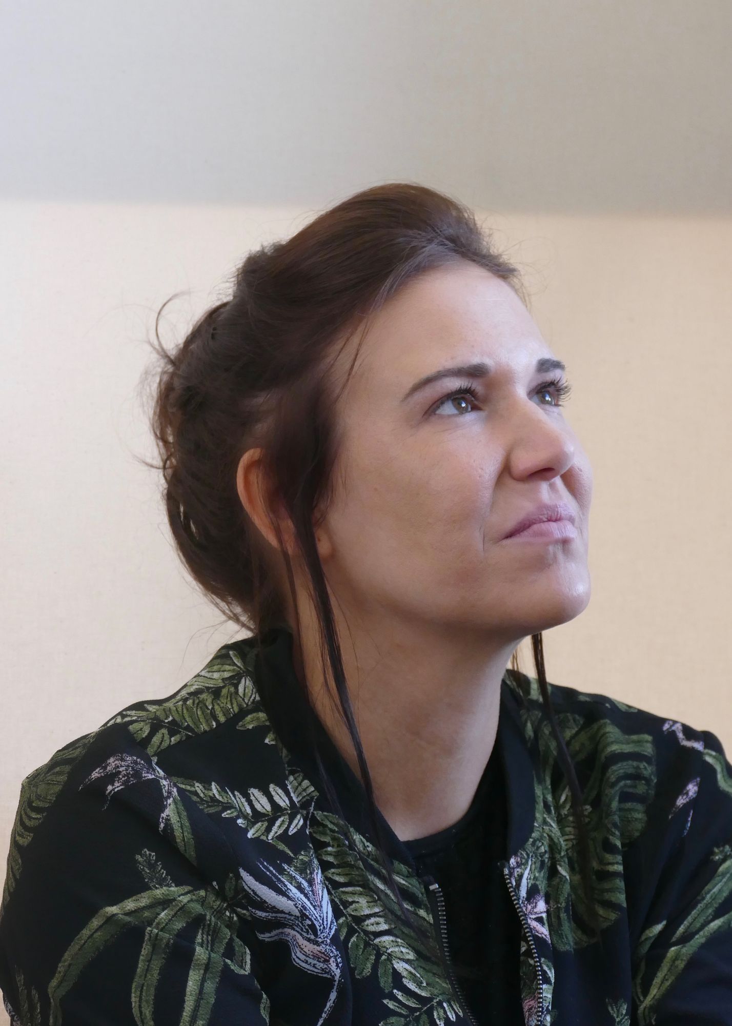 Man sieht eine Frau um die 30 im Potrait, die seitlich fotografiert in die Ferne schaut, Sie hat dunkle Haare, die sie zusammengebunden trägt.
