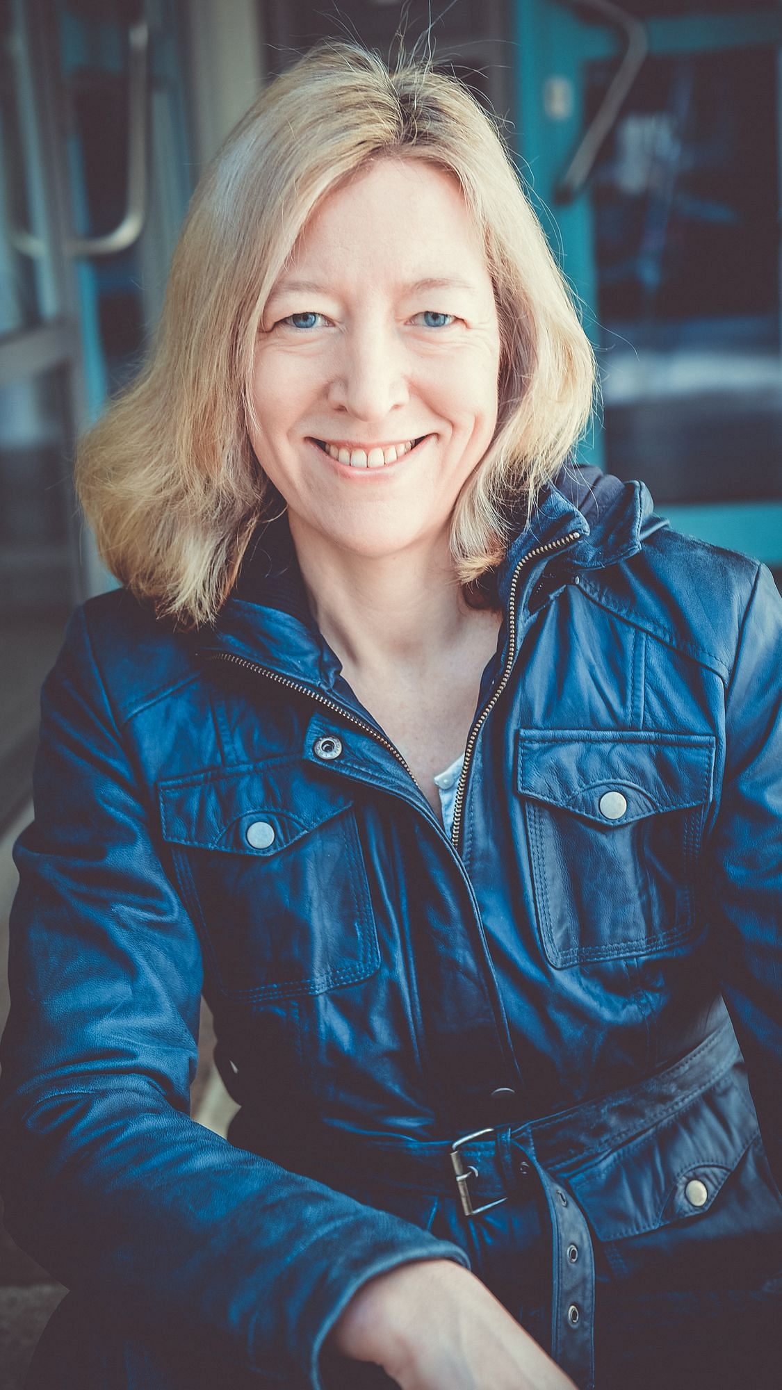 Eine blonde, mittelalte Frau in einer blauen Lederjacke.