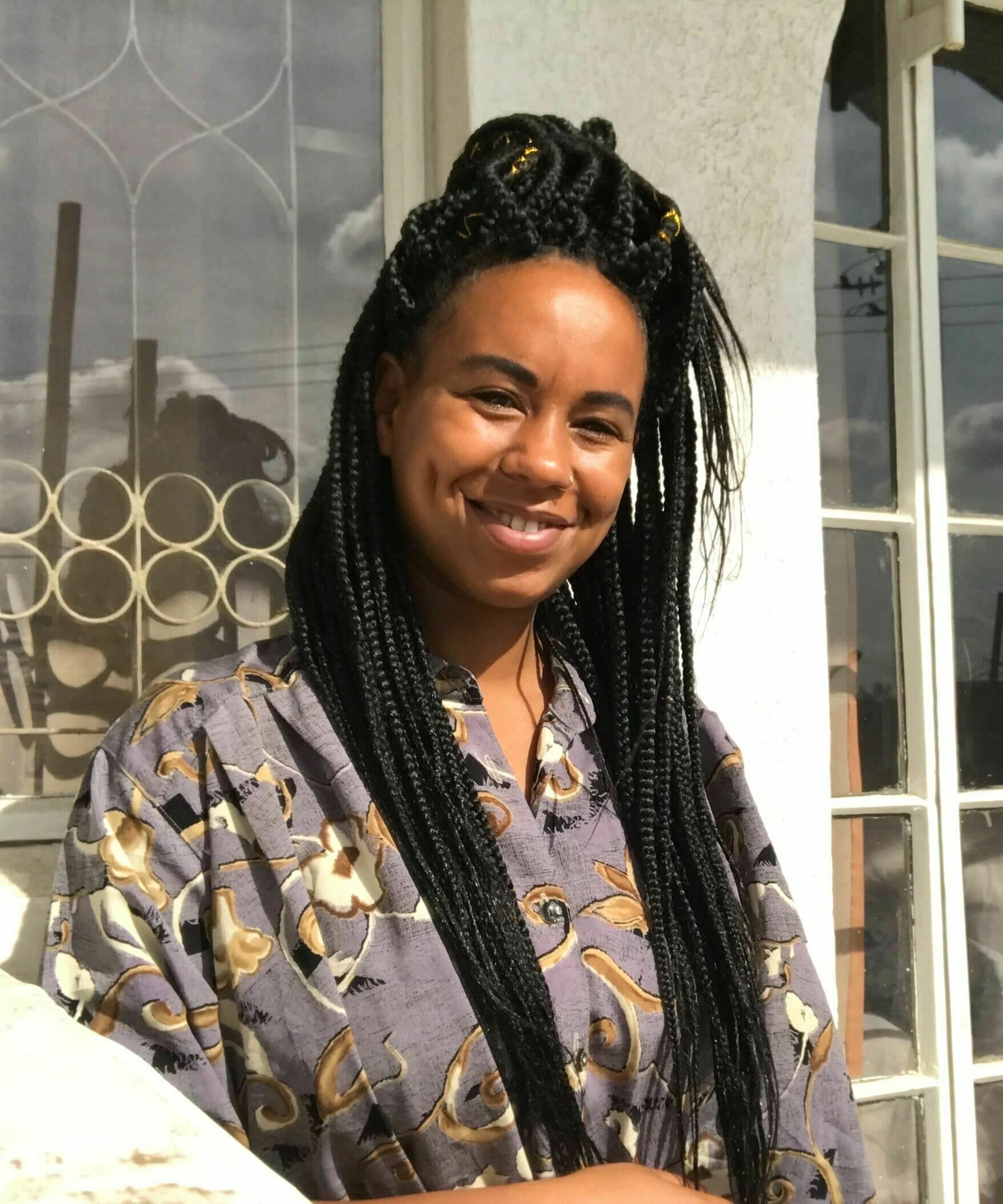 Eine junge Frau mit geflochtenen Zöpfen blickt in die Kamera.