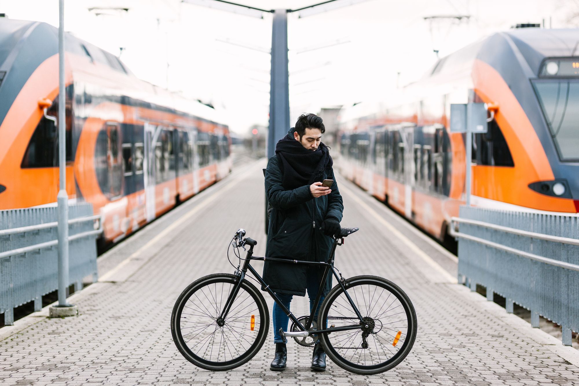 Ein Mann mit Fahrrad steht auf einem Bahnsteig, neben ihm halten zwei Züge.