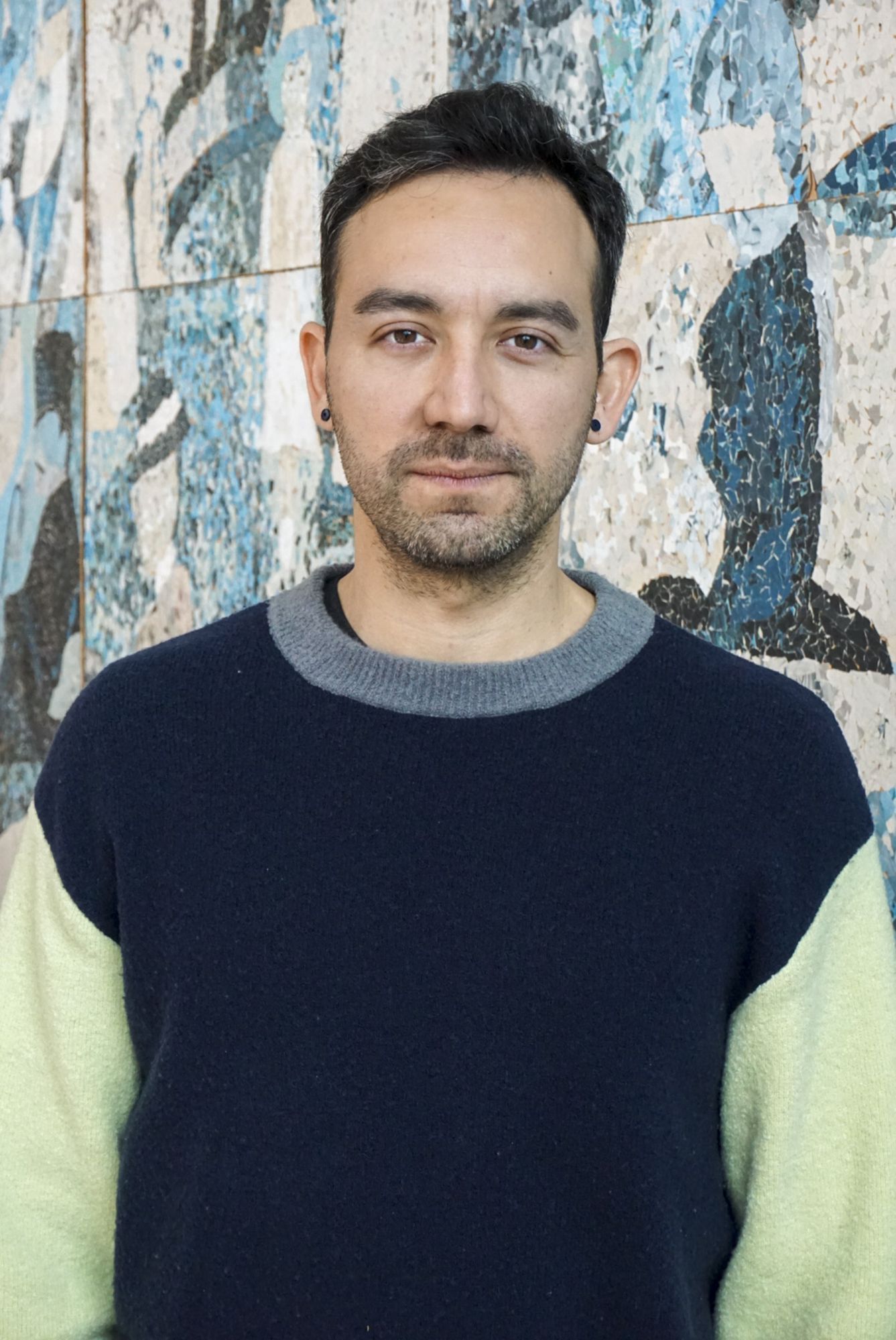 Ein Porträt von David Peña-Guzmán, der vor einer Wand mit einem blau-weißen Muster steht. 