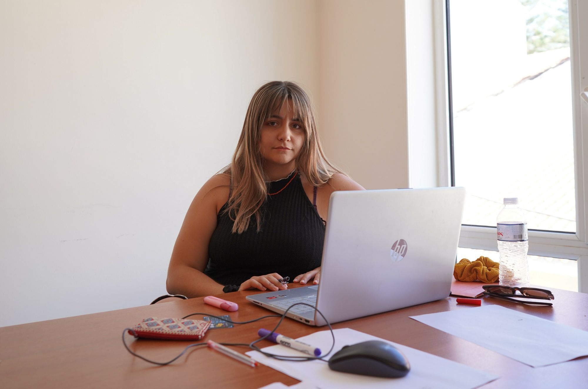 Ioanna Begiazi in schwarzem Kleid an ihrem braunen Holzschreibtisch. Vor ihr steht ein Macbook.
