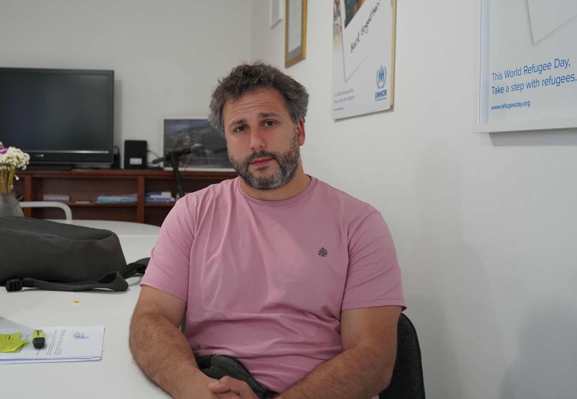 Nikola Kovačević, pinkes T-Shirt, Dreitagebart, sitzt mit gefalteten Händen in seinem weißen Büro in Belgrad.