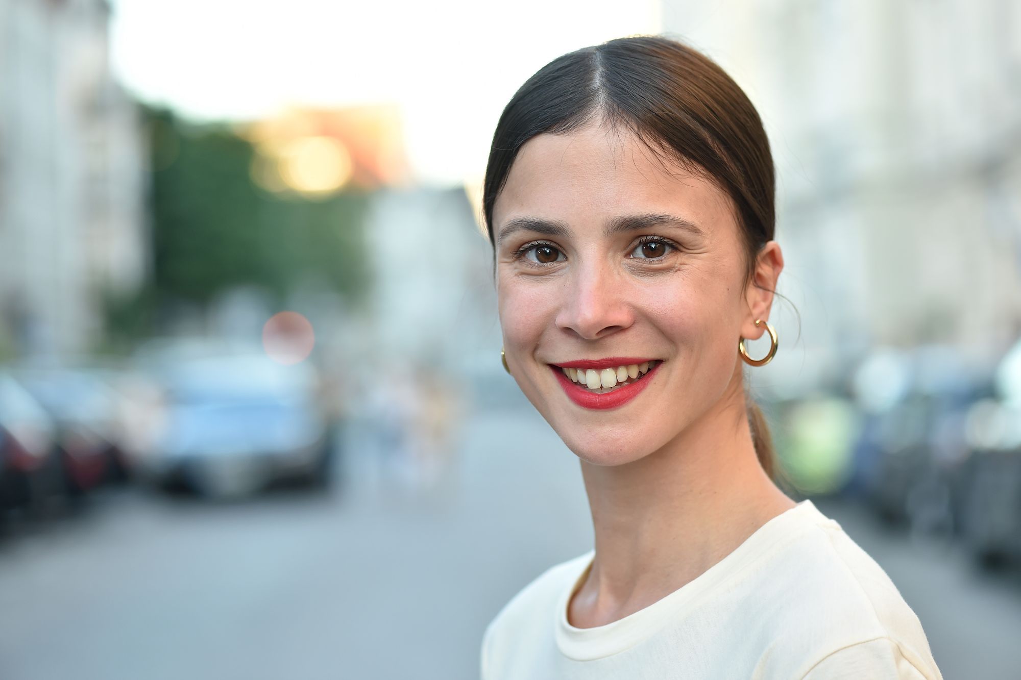 Eine Frau lächelt in die Kamera. Sie hat dunkelbraune Haare und trägt ein weißes Oberteil.