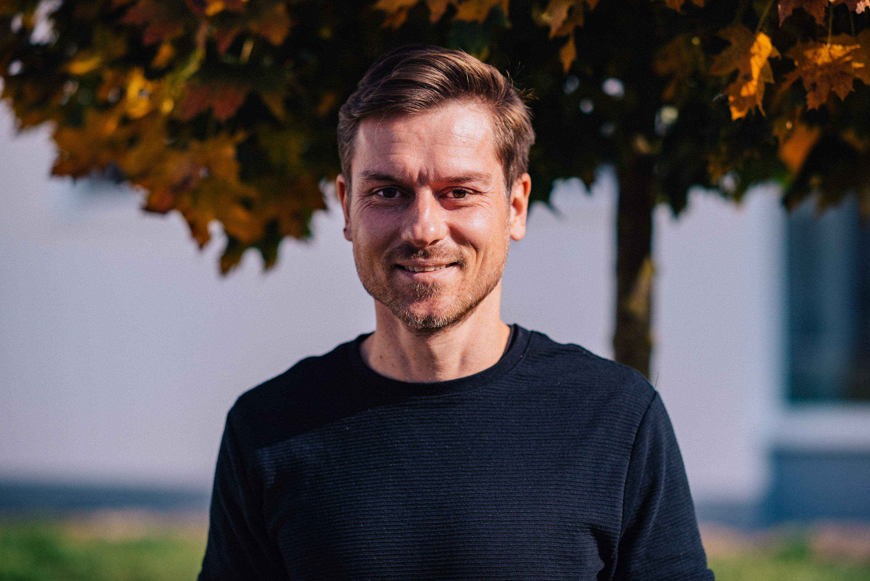 Auf dem Bild ist Pastor Samuel Krauter zu sehen, der freundlich direkt in die Kamera blickt. Er hat kurze, hellbraune Haare und trägt ein einfaches schwarzes Langarmshirt. Sein Lächeln ist leicht und natürlich, und er hat eine ruhige, zugängliche Ausstrahlung.