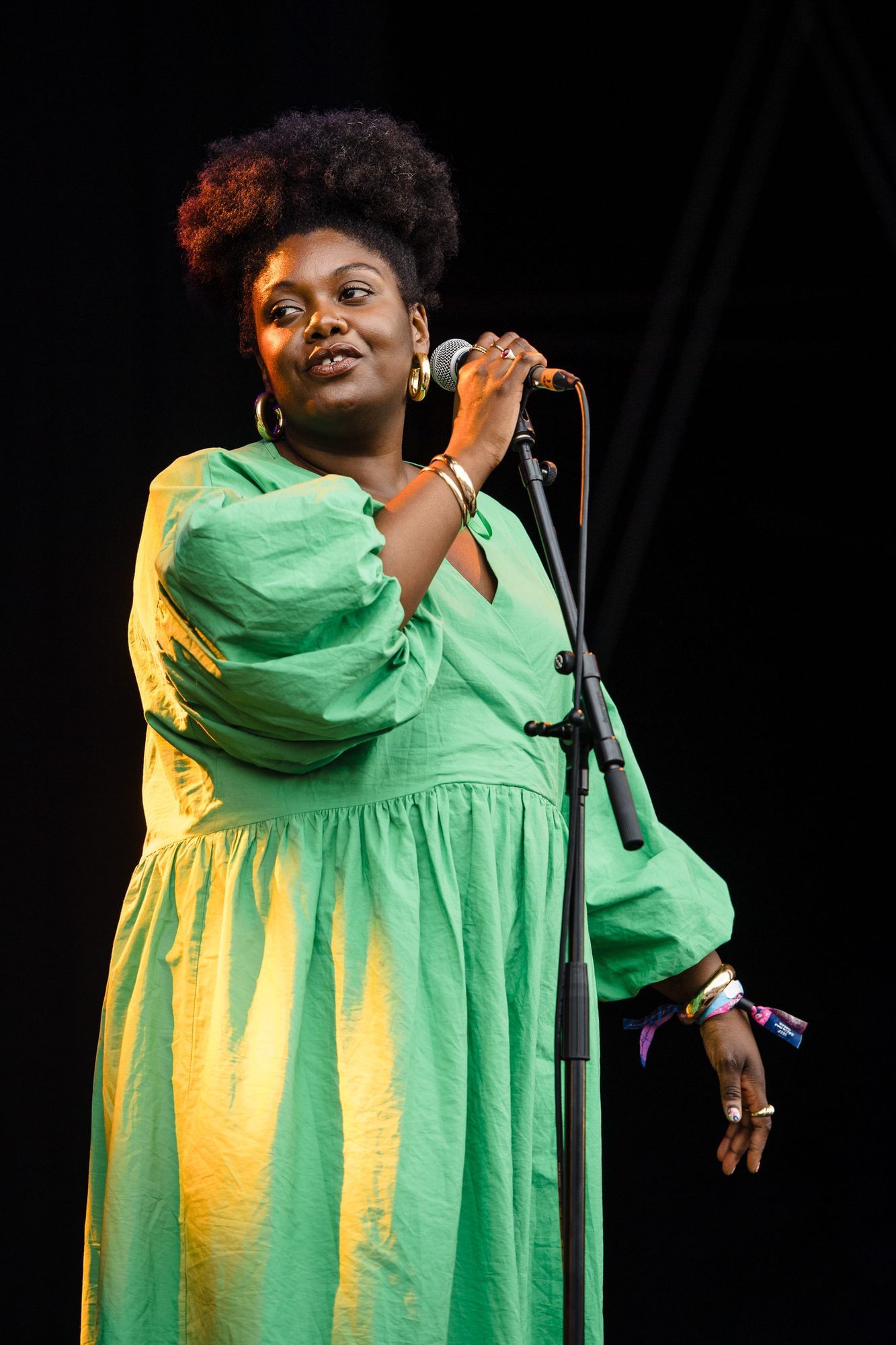 Man sieht die Sängerin Yazmin Lacey, wie sie auf der Bühne singt. Sie trägt ein weites, hellgrüne Kleid, ihren Afro zusammengebunden und goldene Creolen.