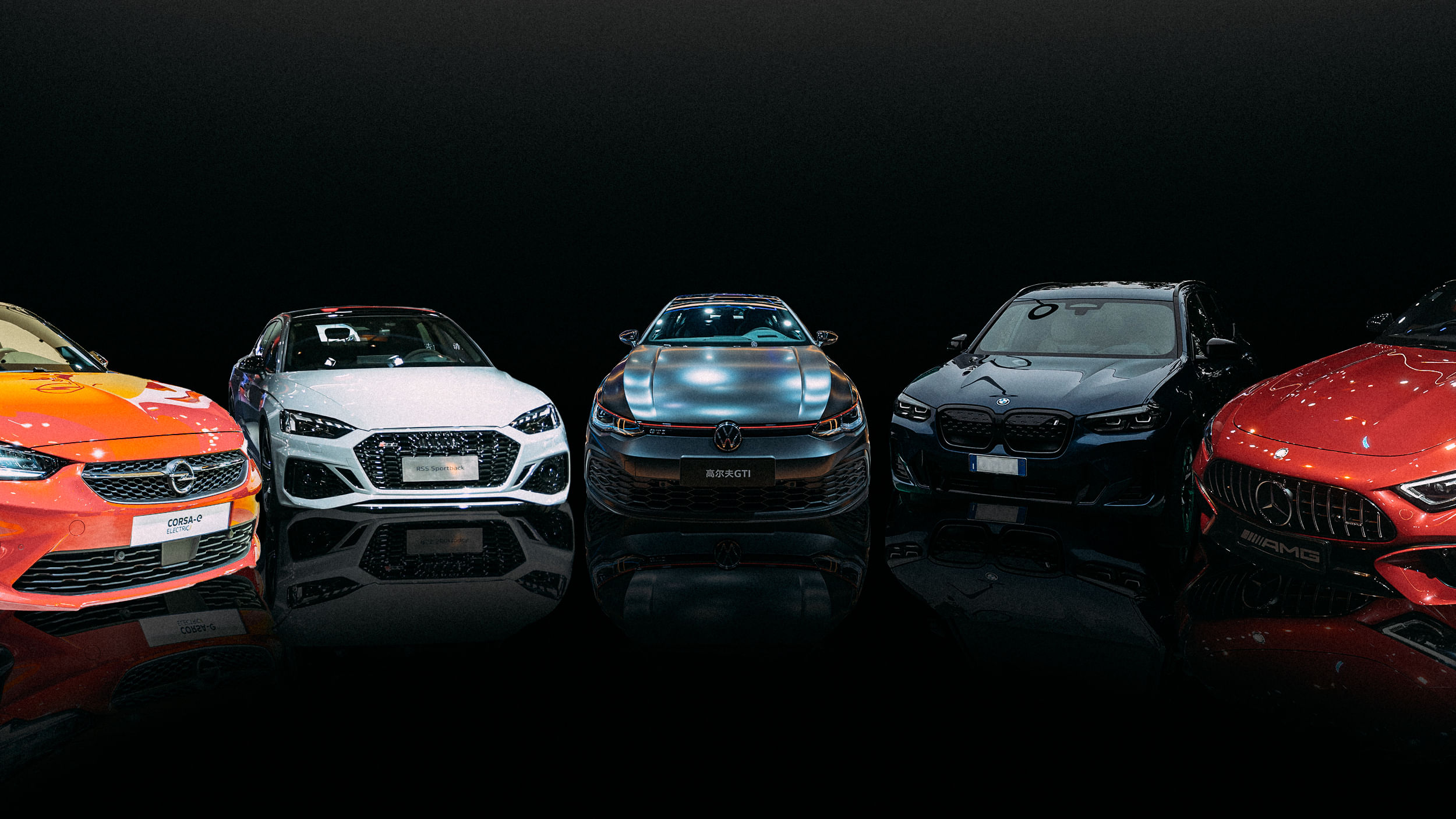 Eine Reihe von fünf verschiedenen deutschen Autos präsentiert nebeneinander, mit der Front zum Betrachter gerichtet. Jedes Auto hat eine andere Farbe, von links nach rechts: Orange, Weiß, Blau, Schwarz und Rot.