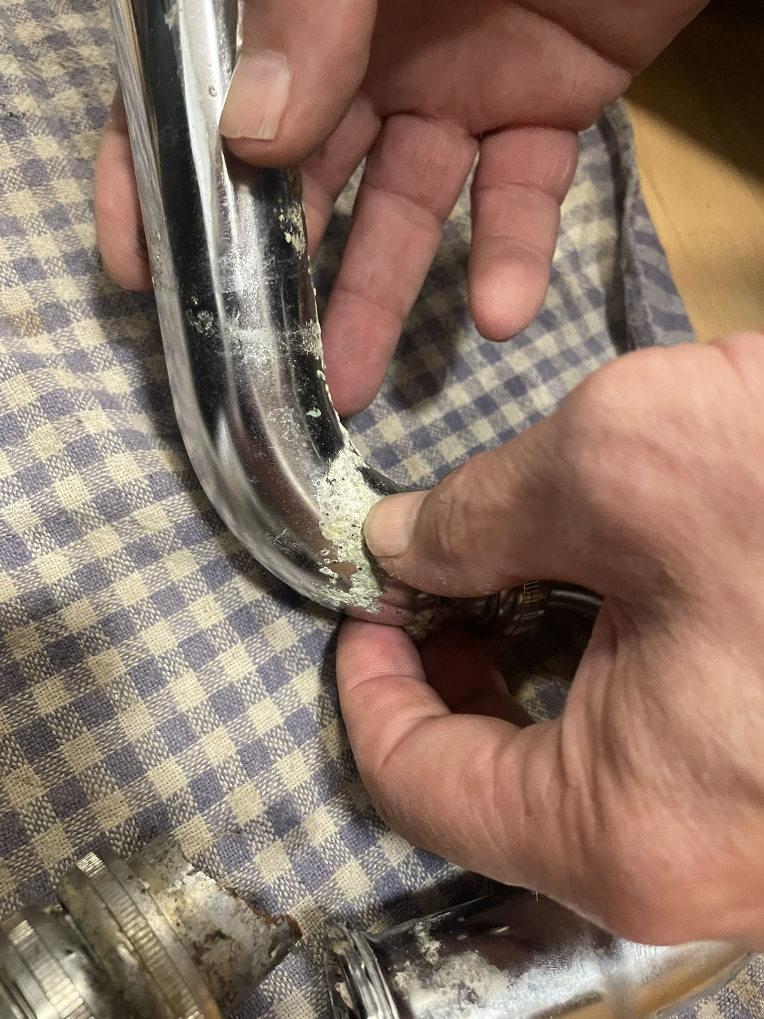 Die Hände meines Klempners, wie sie einen ausgebauten Siphon halten, der offenbar durch Reinigungsmittel porös geworden ist.