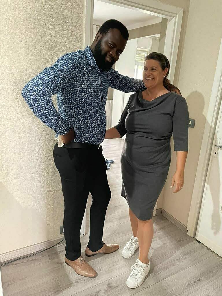 Daniela und Steven stehen end beisammen, sie lächeln in die Kamera. Daniela trägt ein graues Kleid, Steven trägt eine dunkle Hose und ein blau gemustertes Hemd.