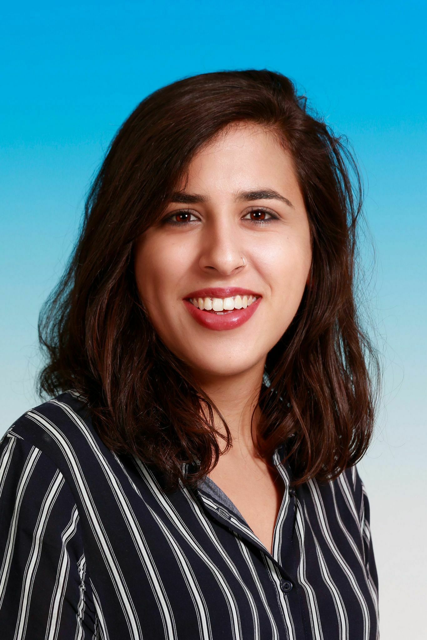 Das Bild zeigt Shahed Bishara. Sie hat lange dunkle Haare, lächelt freundlich und trägt ein gestreiftes Hemd.