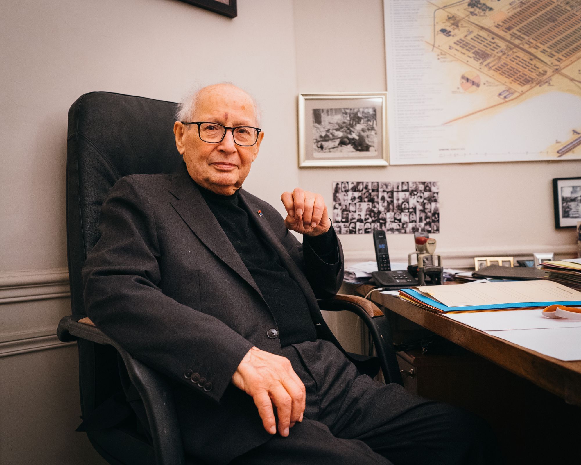 Serge Klarsfeld sitzt in seinem Schreibtischstuhl und blickt in die Kamera. Er trägt eine Hornbrille. In Hintergrund erkennt man Fotos an der Wand.